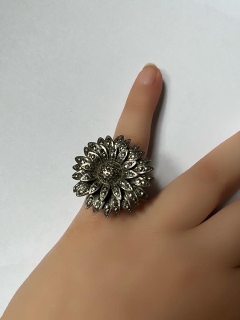 Delicatamente realizzato in argento, questo affascinante anello a forma di margherita presenta due file di petali ornati da strass scintillanti, che si irradiano intorno a un cuore centrale incastonato. Il timbro del cigno garantisce l'autenticità e