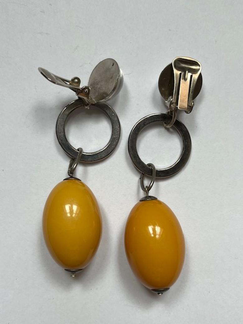 Designed by the iconic Roger Scemama, this elegant pair of clip-on earrings is a beautiful fusion of vintage charm and bold design. Crafted from silver-toned metal, each earring features a sleek circular element with a transparent glass cabochon