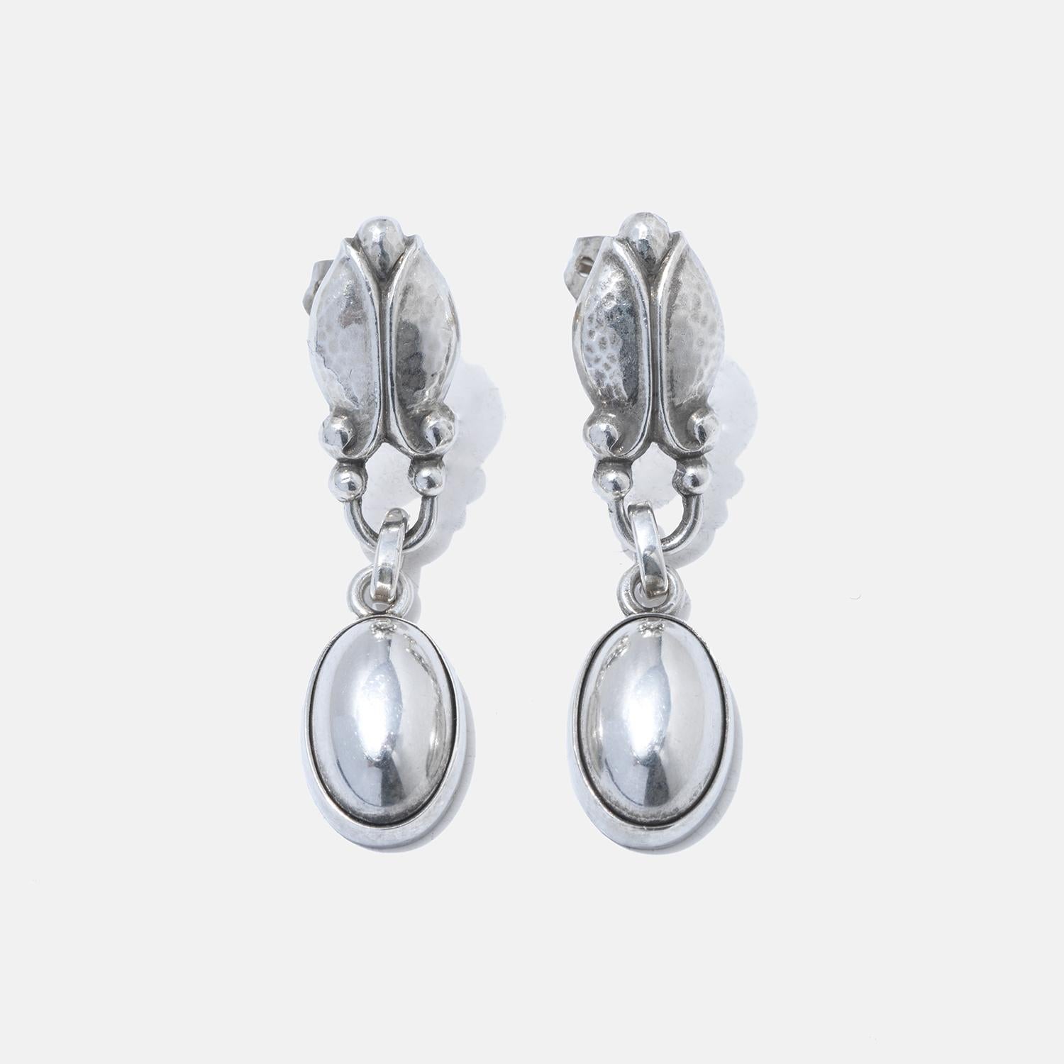 These sterling silver earrings showcase a delicate leaf pattern at the top with a hammered finish that provides texture and visual interest. Attached to the leaf motif by a small, articulated joint is a smooth, polished oval drop that sways gently,