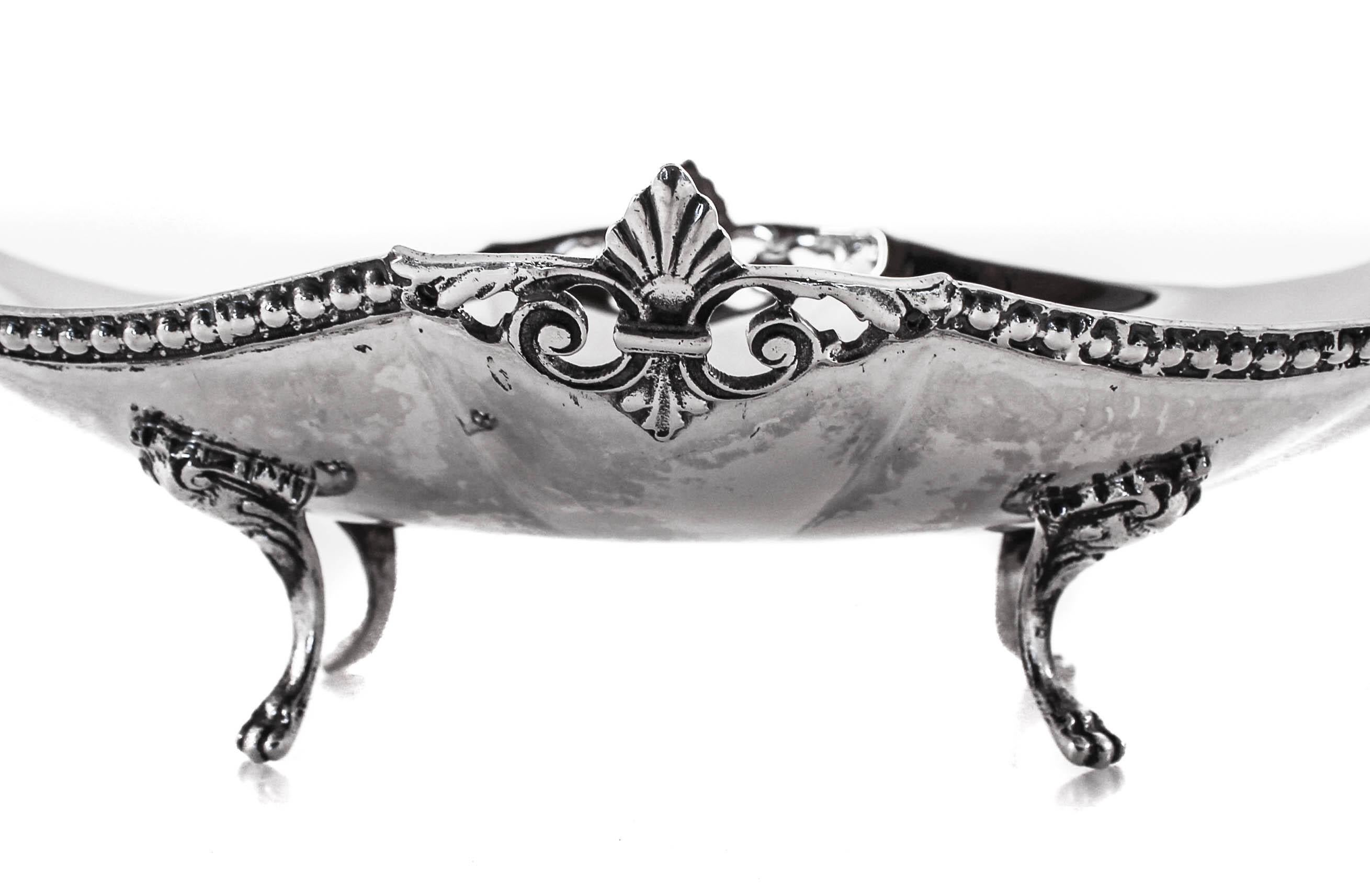 Standing on four claws, this oval sterling silver dish is lifted off the surface. On opposite ends a curler handle makes it easy to carry and pass around. The inside is clean and without ornamentation however along the outside rim there is a