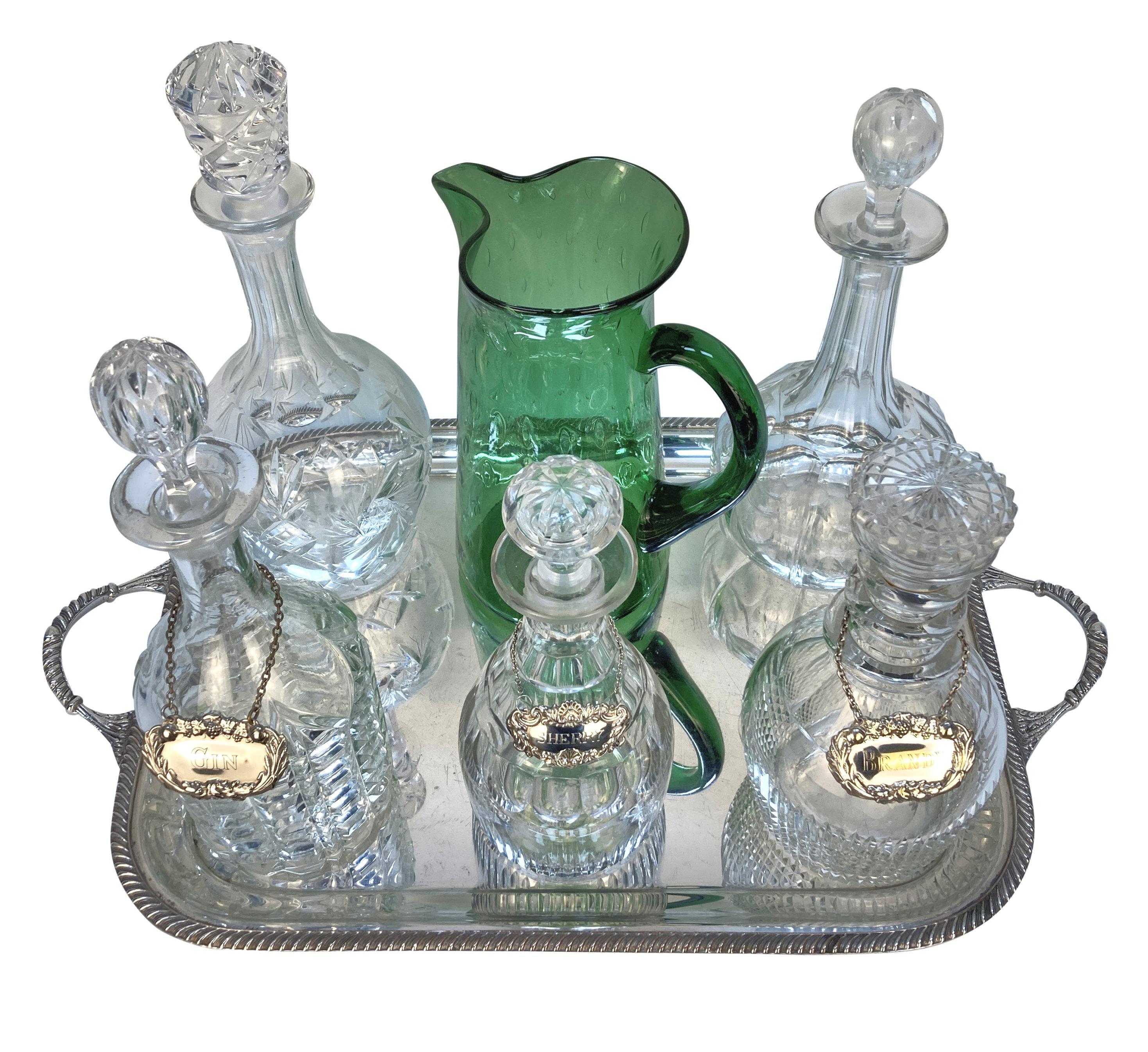 Ein englisches versilbertes Getränketablett, auf dem fünf geschliffene Glaskaraffen verschiedener Größe stehen, drei davon mit silbernen Getränkeetiketten. Außerdem gibt es einen mundgeblasenen Wasserkrug aus grünem Blasenglas aus der