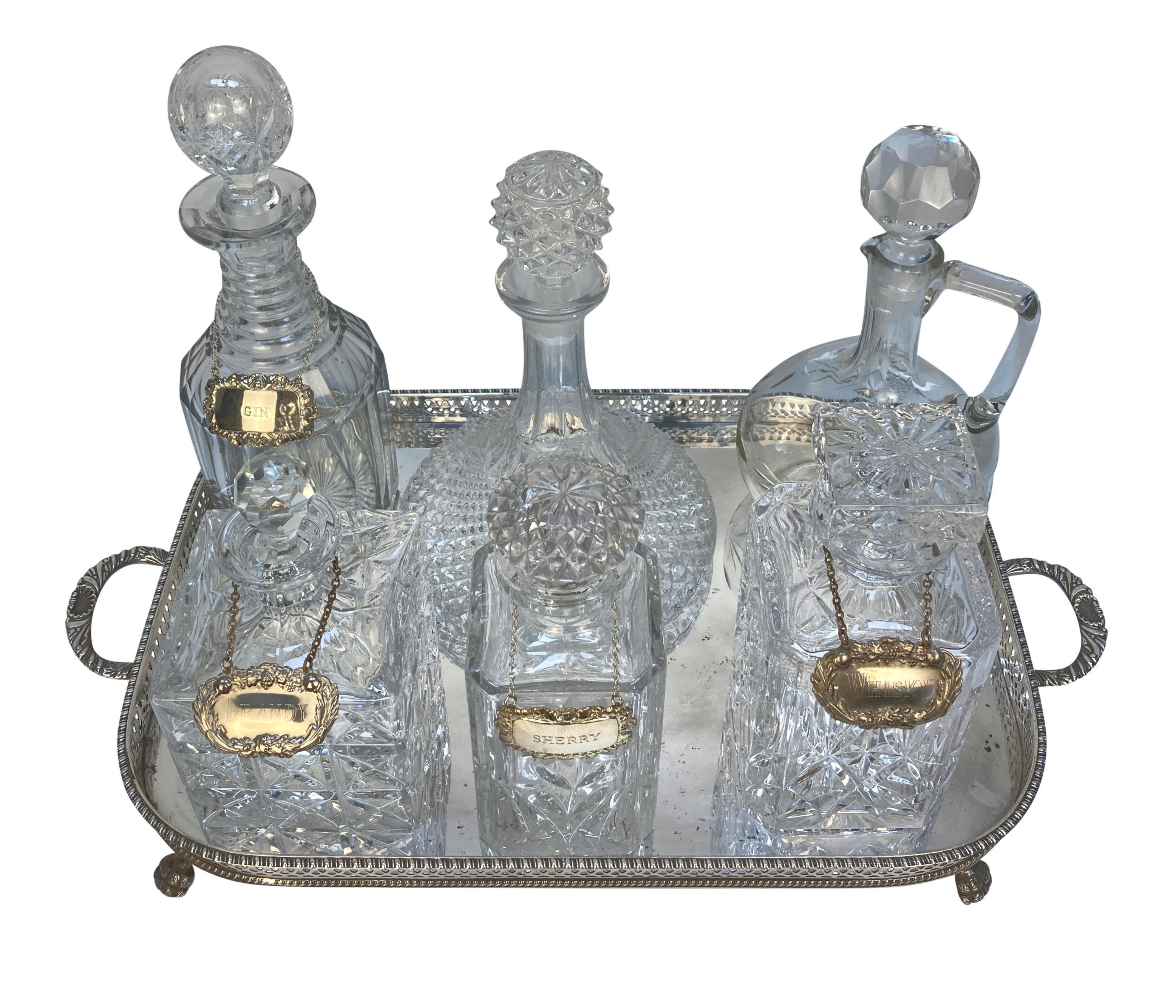 Un plateau à boissons anglais en argent plaqué, à galerie, sur des pieds en pattes de lion, supportant six carafes en verre taillé de différentes dates, de la fin du XIXème siècle au début du XXème siècle. Quelques carafes portant des étiquettes en