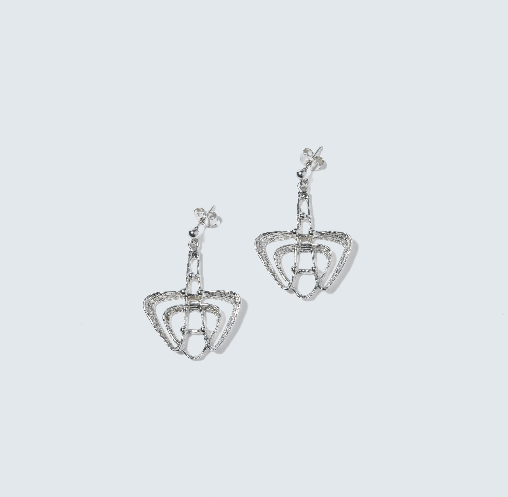 These are sterling silver dangling earrings with a patterned surface finish. The lower part of the earrings forms a triangle with sizeable, hollowed-out spaces, giving a modern geometric look. Above the triangles, the earrings feature a chain of