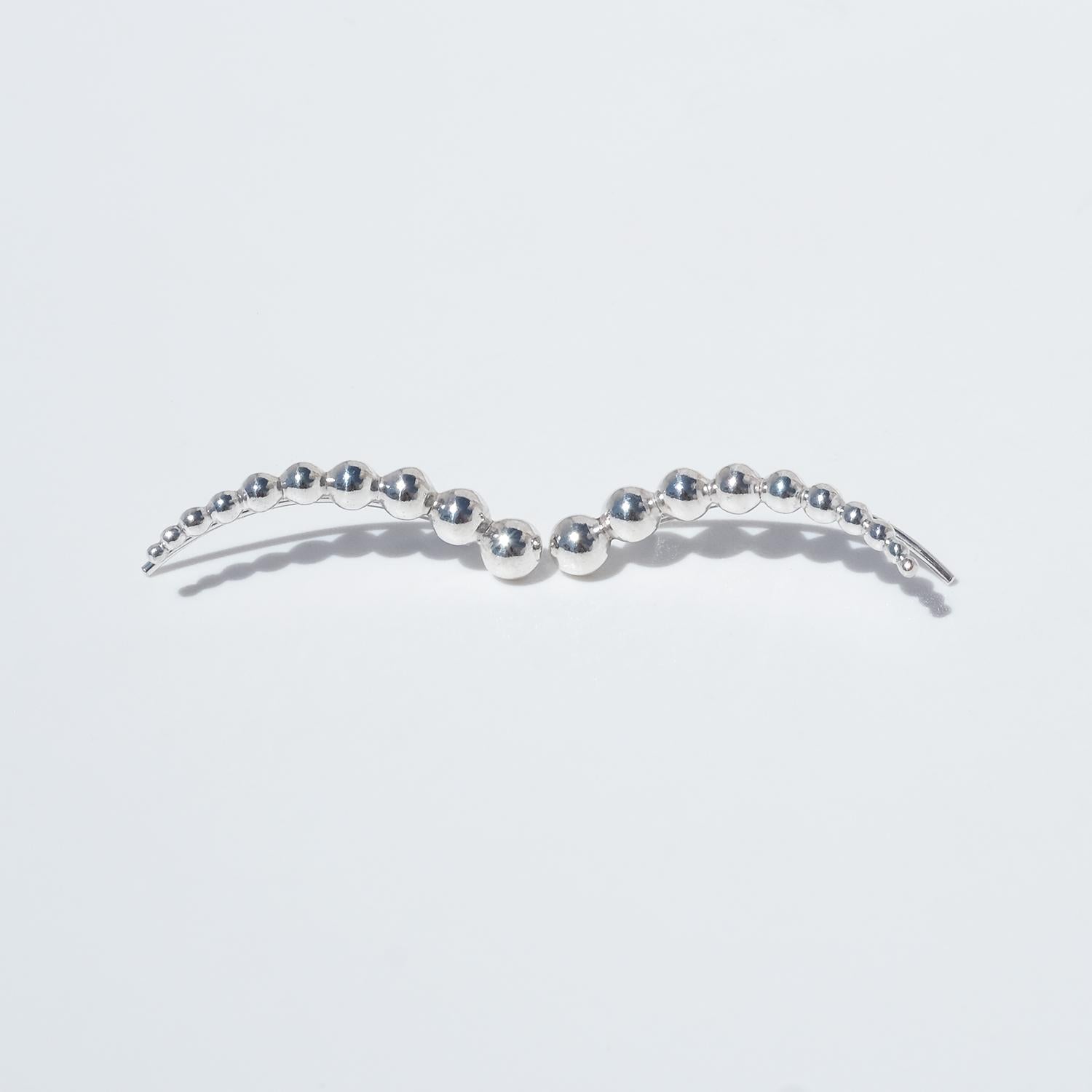 These sculptural sterling silver earrings are part of the Moonlight Grapes collection. Each earring features a graceful arc of polished silver spheres, arranged in descending size from top to bottom—evoking a stylized, abstracted grapevine. The