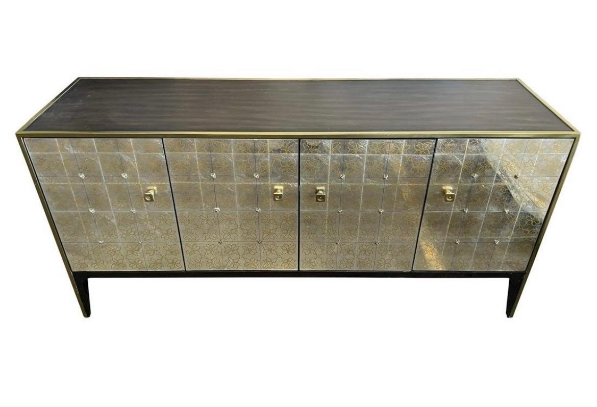 Stunning four door credenza sideboard features an eglomise mirrored front with a gold floral pattern and brass pulls. The shelves are adjustable. Top and sides are a wood veneer with brass trim all around.
Can also be used as an entertainment