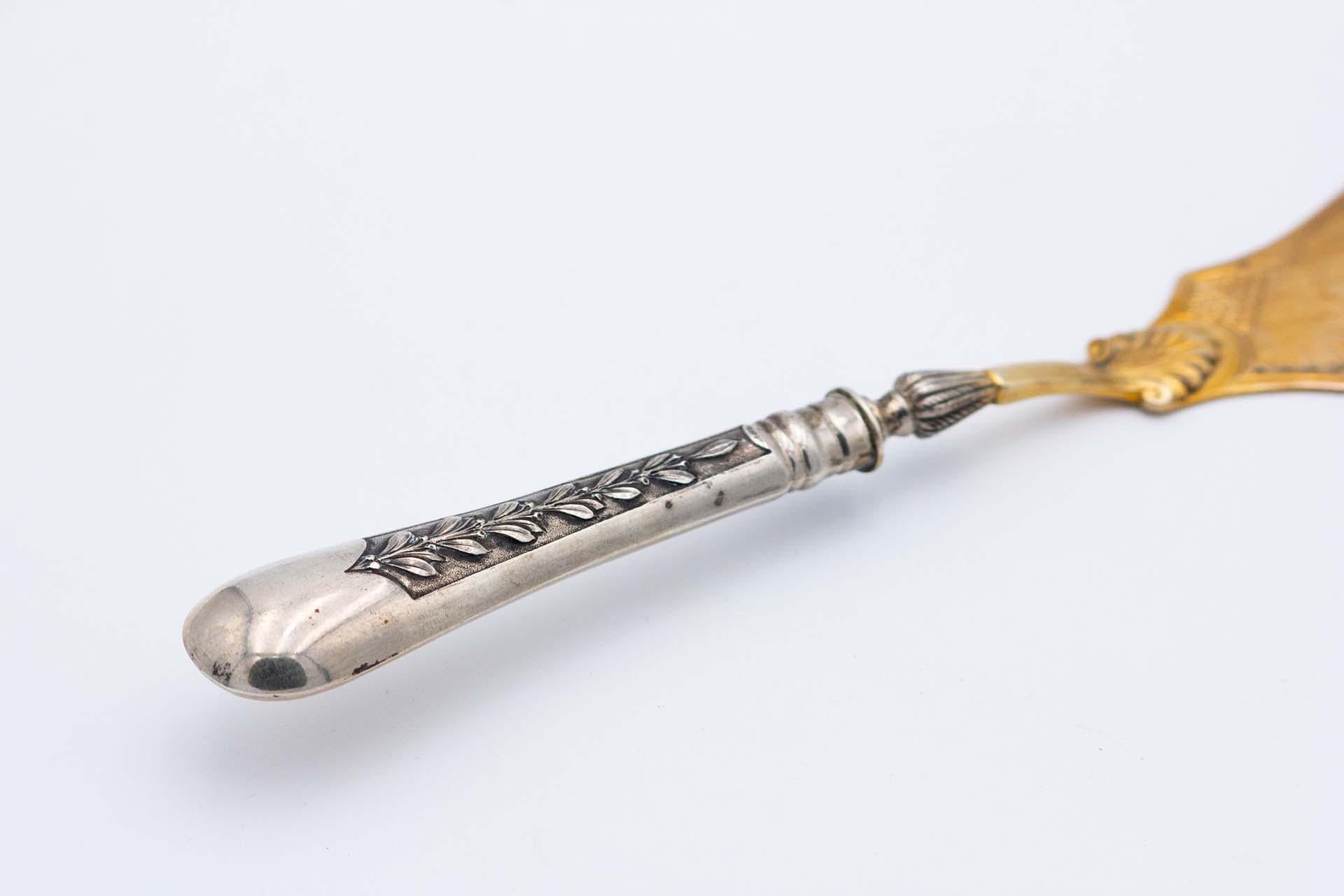 Description: Silver fish knife with floral motifs engraved on the gold blade and embossed handle. Metal: Silver. Origin: Portuguese. Brand: boar II Title. Weight: 107.67 grams. Dimensions: 29.2cmx1.6cm. Content: 833/1000. Assay Mark: Yes, between