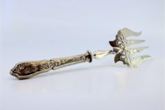 Silver fish serving fork with floral design, four prongs and raised handle