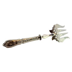 Silver fish serving fork with floral design, four prongs and raised handle