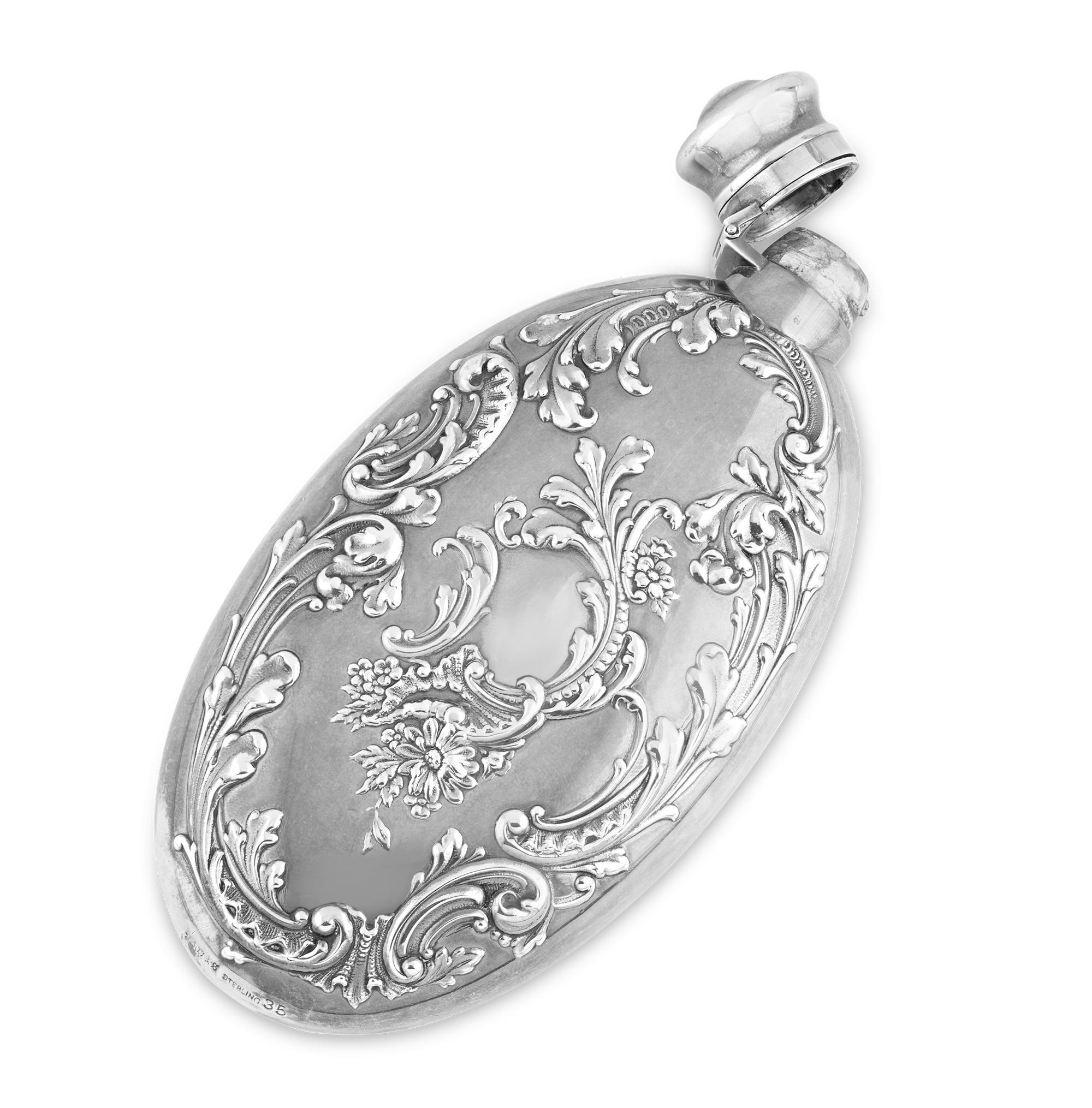 This delightful and ornate oval sterling silver flask crafted by prolific American silversmiths R. Wallace & Sons features a beautiful repoussé filigree pattern. Punctuated by blooming flowers, this flask makes a lasting impression. Known for their