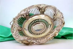 Silver fruit bowl w/ cutouts & reliefs, hinged handle resting on a circular base