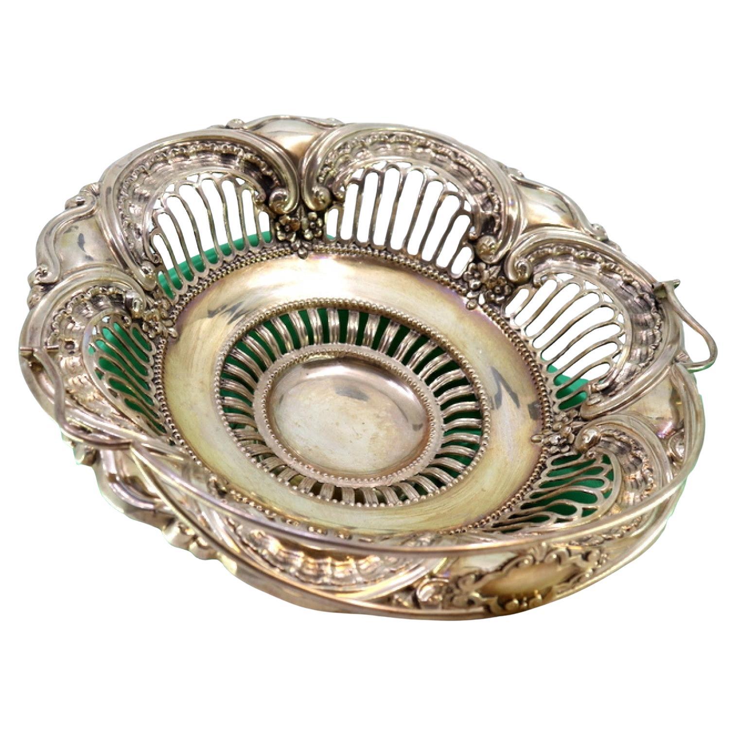 Silver fruit bowl w/ cutouts
reliefs, hinged handle resting on a circular base