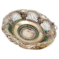 Silver fruit bowl w/ cutouts
reliefs, hinged handle resting on a circular base