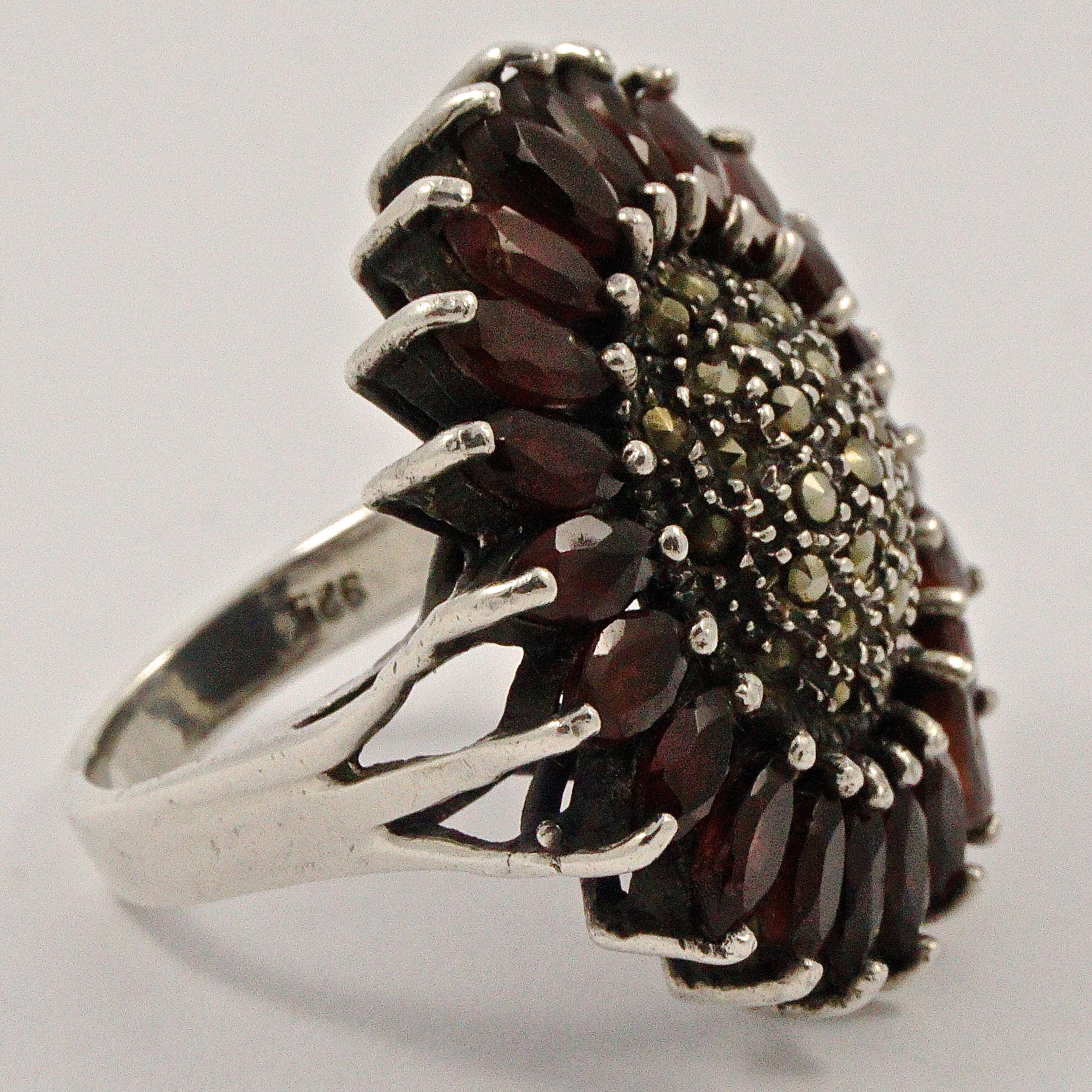 Silver statement ring featuring a lovely flower design set with garnets and marcasites. Ring size UK O 1/2, US 7 1/4, inside diameter 1.85cm / .72 inch. The front measures diameter 3.1cm / 1.22 inches. The back and sides are finished with a black