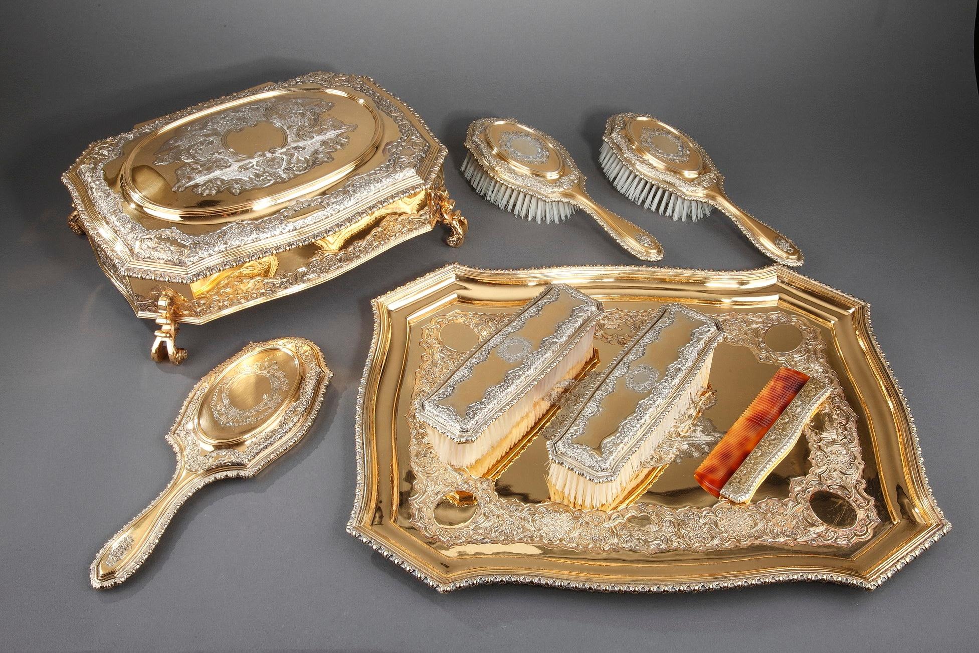 George V dressing-table service crafted of silver-gilt, comprising an oblong tray, a large jewel box with detachable velvet lining, two hair brushes, two clothes brushes, a comb and a hand mirror, all contained in a fitted red leather covered case.