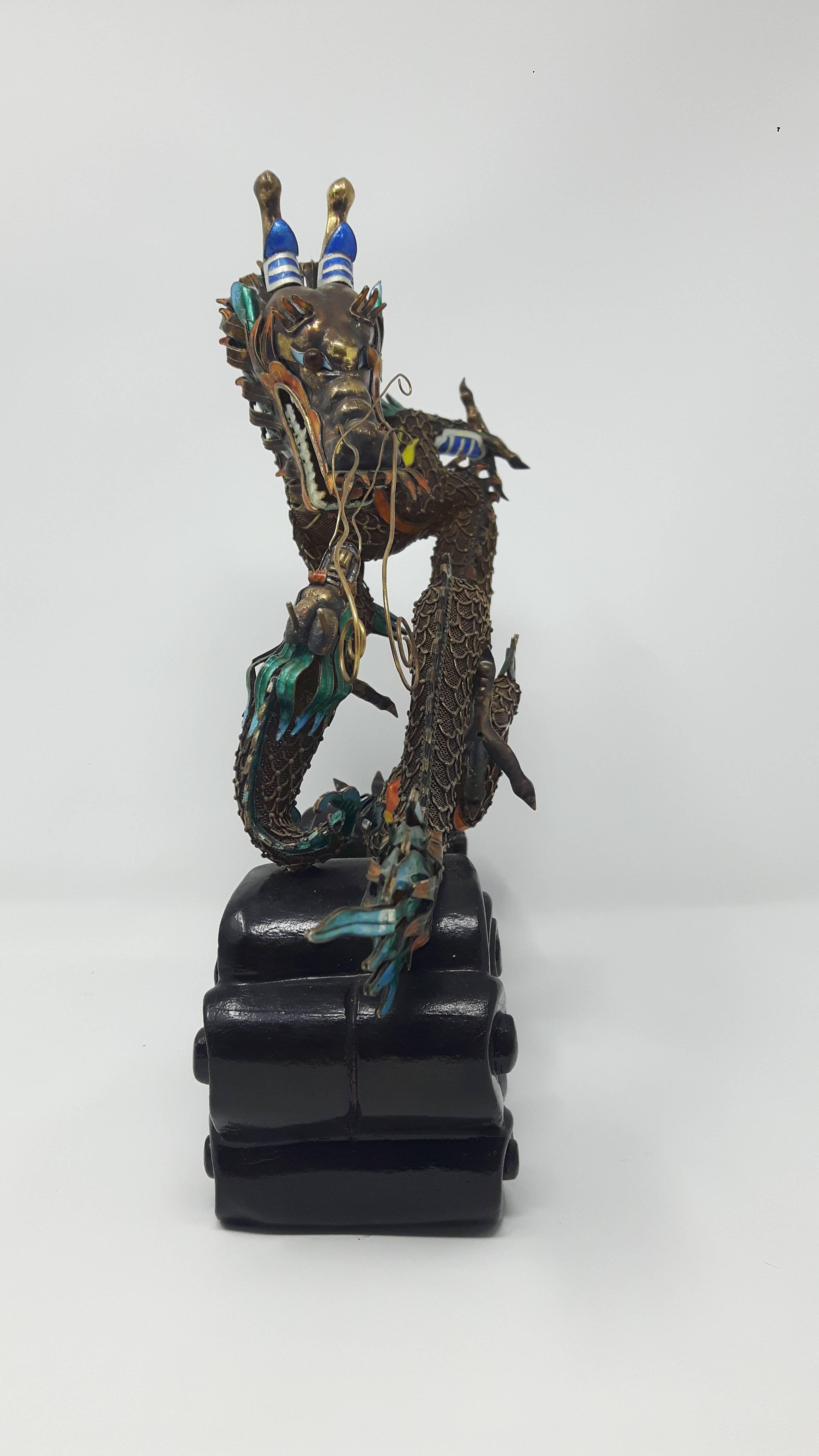 Early 20th century.
Formed as a writhing dragon confronting a dragon- fish, the head and fins of both animals decorated with coloured enamels, on carved and lacquered wooden base formed as waves, the underside of one claw applied with a plaque