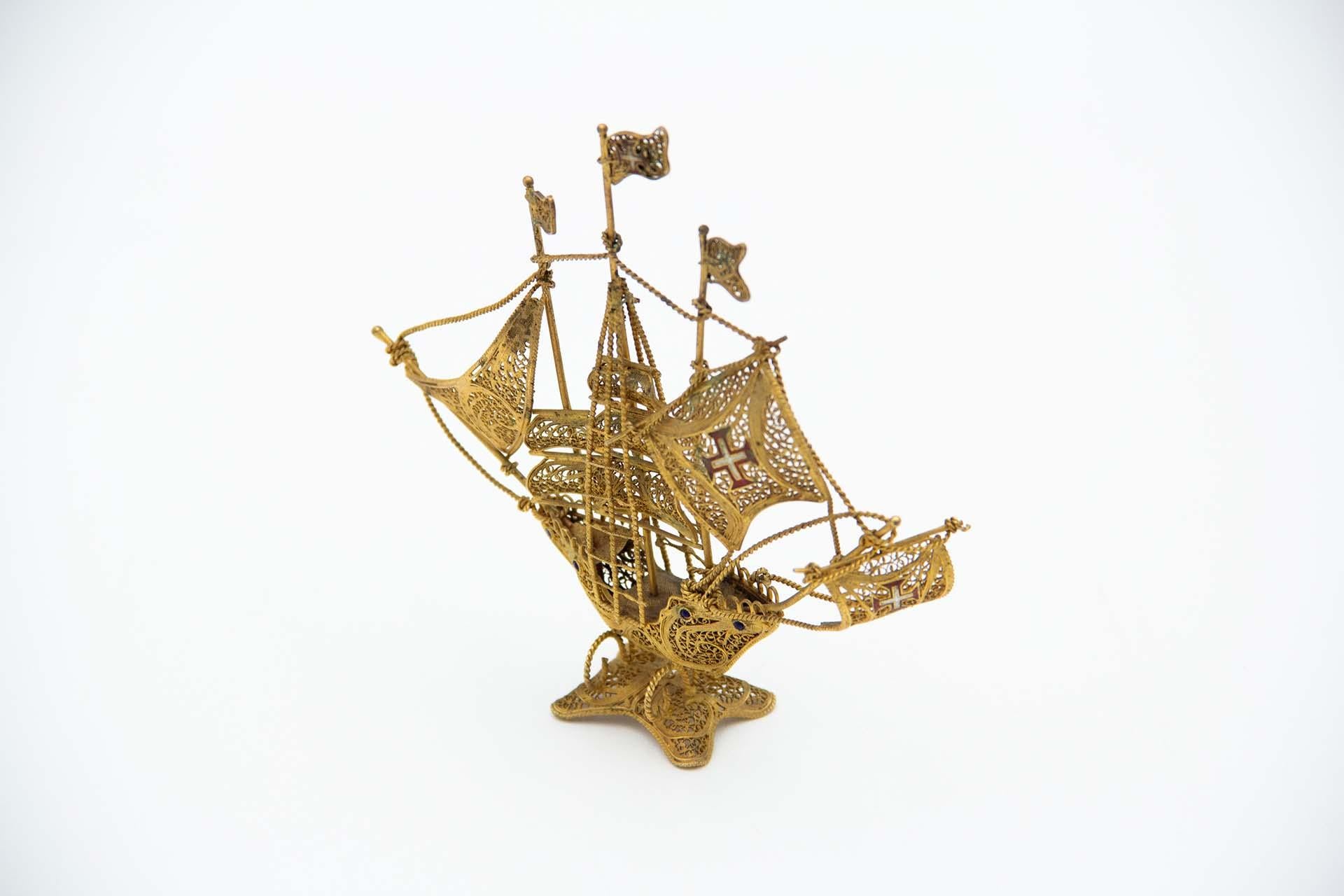 Description: Miniature silver-gilt caravel with filigree mesh and polychrome crosses. Metal: Silver. Origin: Portuguese. Brand: Eagle Head. Weight: 42.89 grams. Dimensions: 12cmx12.5cm. Content: 833/1000. Assay Mark: Yes, between 1938 and 1984.