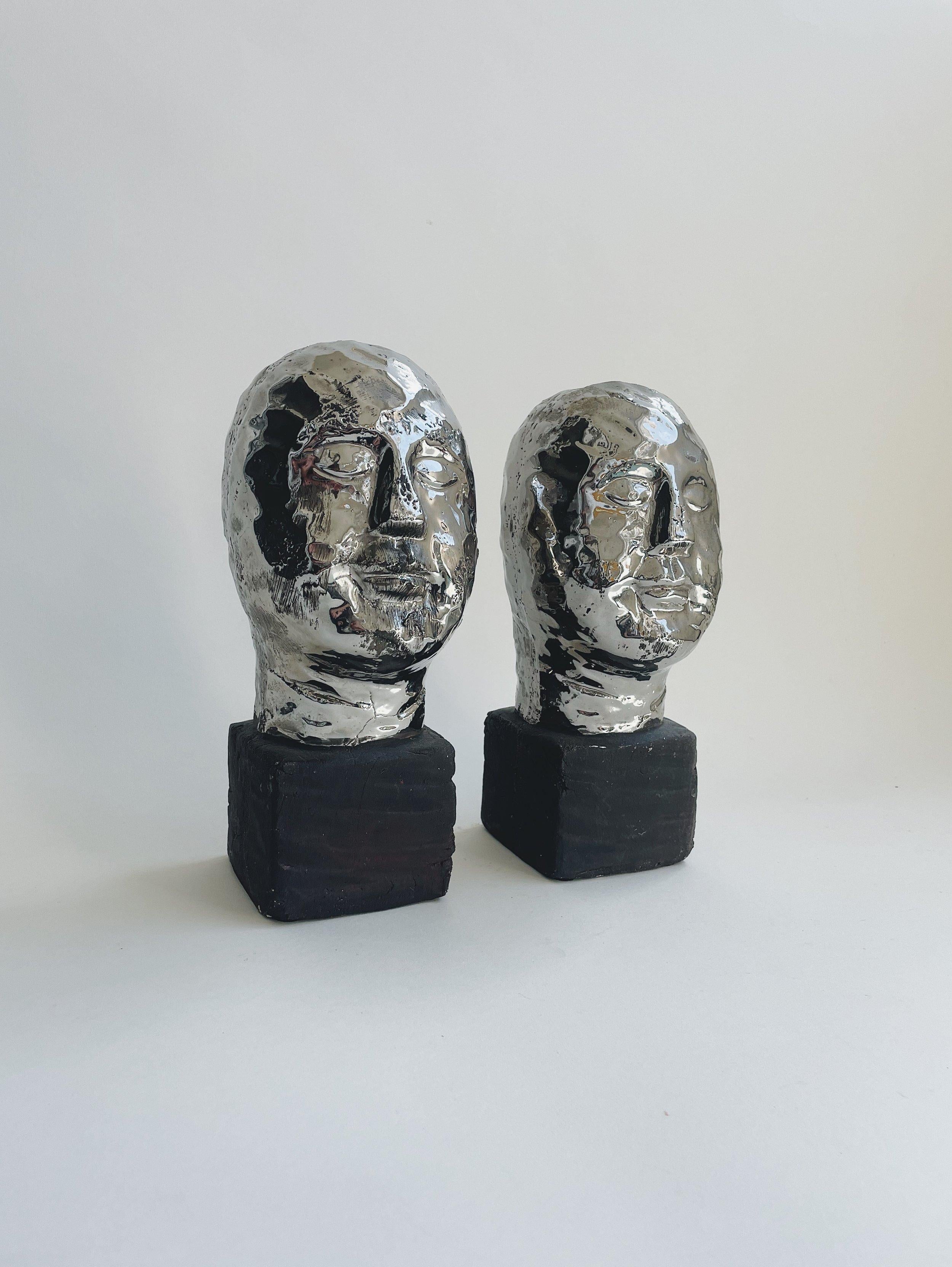 Studio pottery

Remarkable pair of studio pottery busts. Simple, almost Cycladic style faces sit atop a matte brown glazed cube. Sculpted as a single piece of pottery. Faces are glazed in a reflective silver. Sold as a pair.

Each pieces has a
