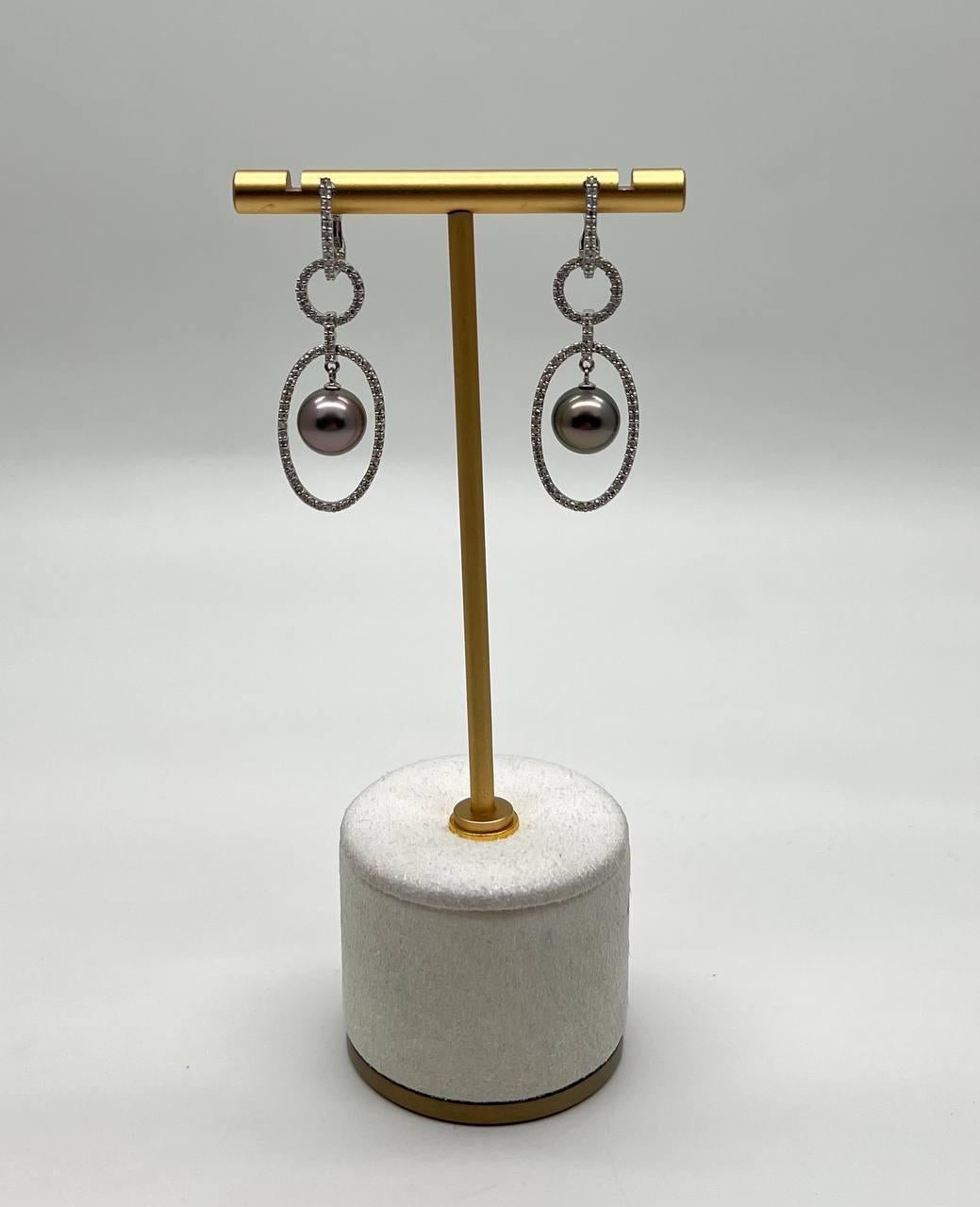 This exquisite pair is crafted with precision, featuring a delicate design of interlocking circles adorned with sparkling diamonds. Each earring showcases a lustrous pearl suspended within an oval frame, adding a touch of sophistication. The
