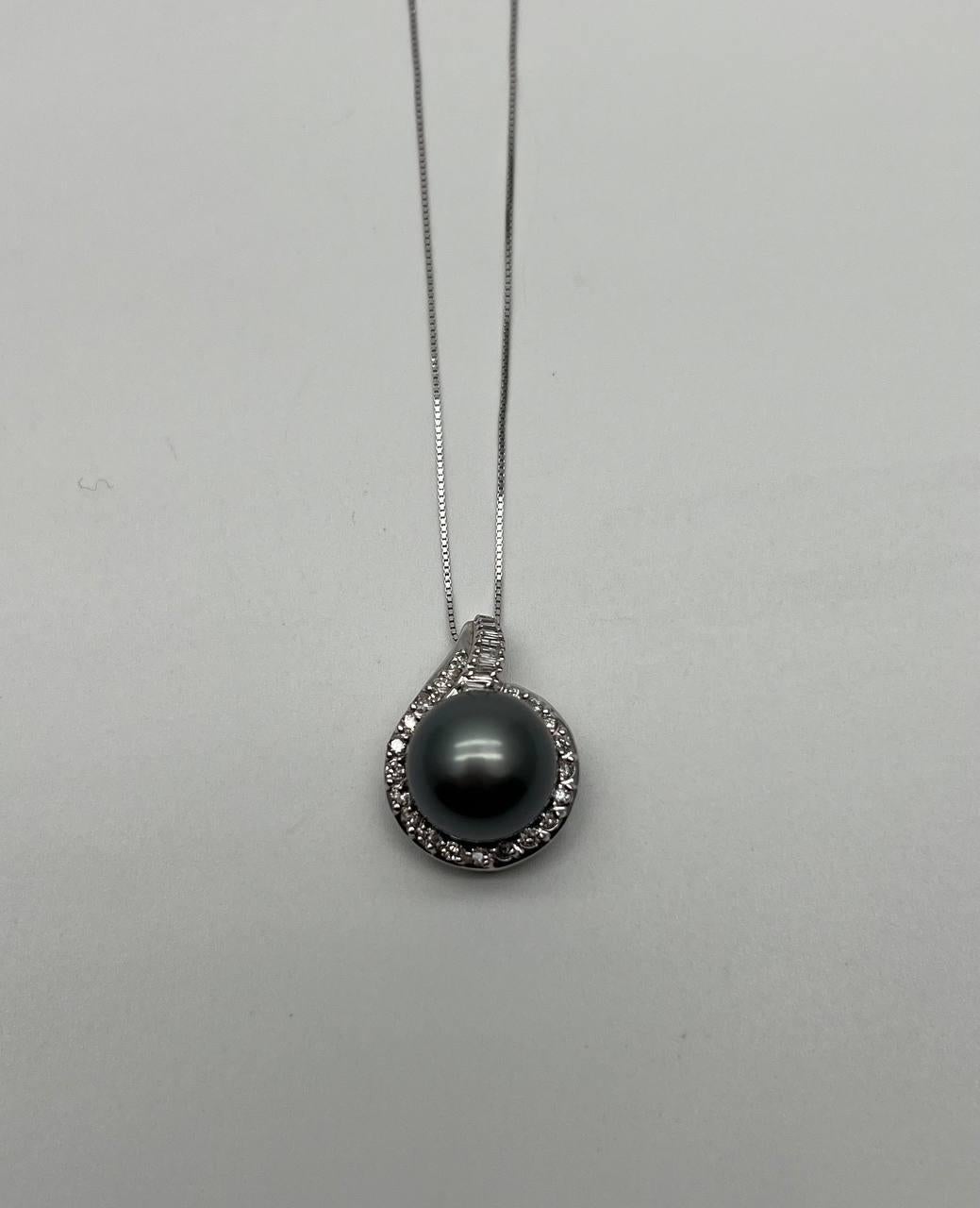 Pendant necklace featuring a central black Tahitian pearl encircled by a halo of round brilliant-cut diamonds and baguette cut diamonds on the top bail. Suspended on a sleek 14K White Gold Chain. 
Natural Pearls and Diamonds.