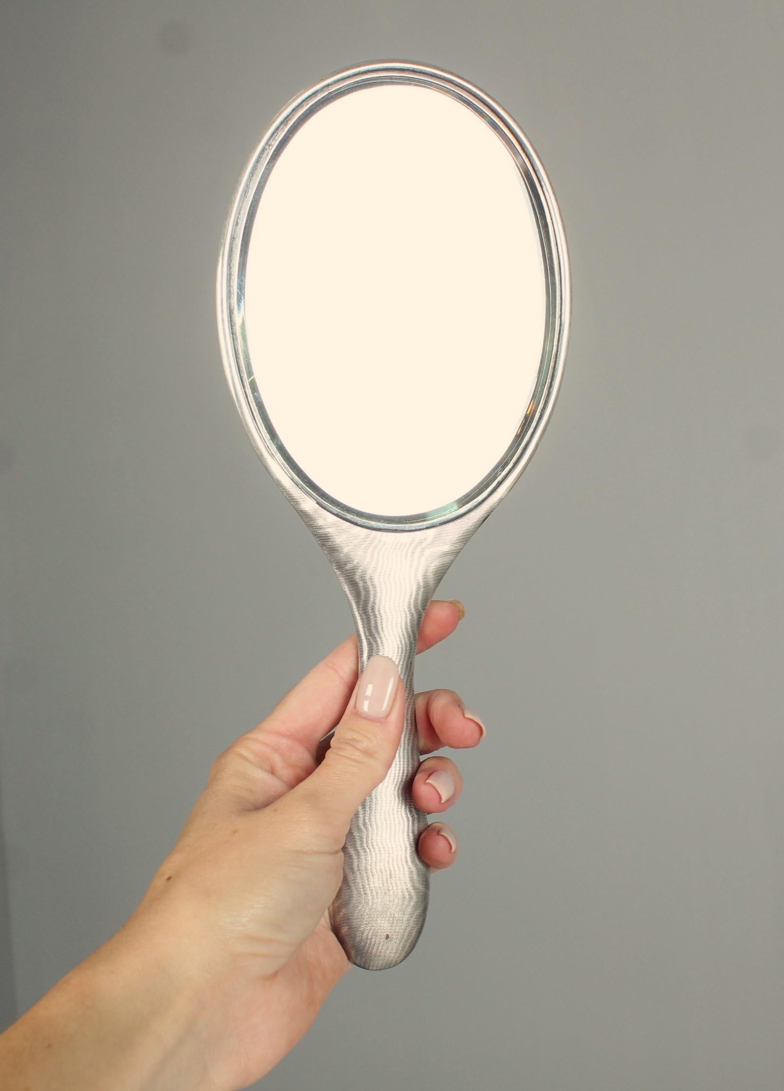 English hand mirror with guilloch´s moirée trompe l´oeil.
Stamped 925 silver.
Birmingham, 1909.
Provenance of the collection of Karin Szekessy and Paul Wunderlich, from Hamburg.
