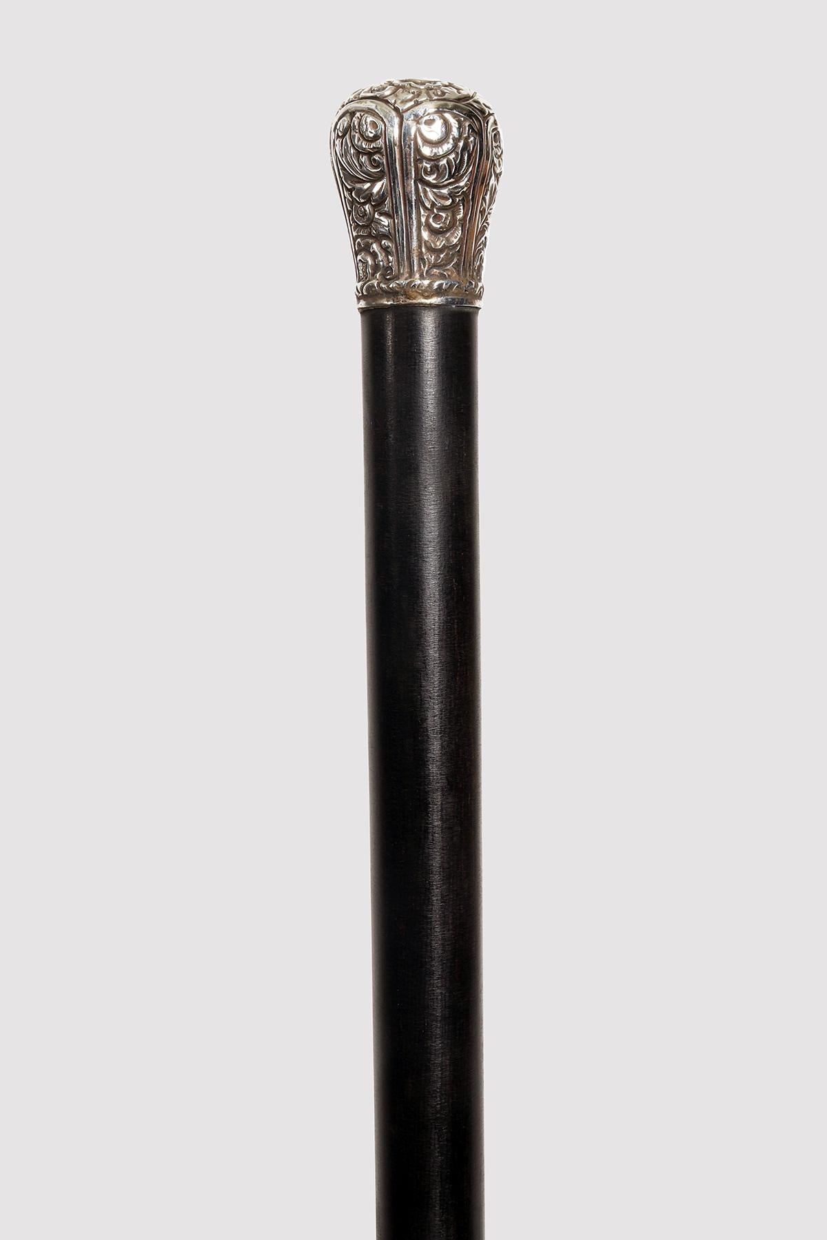 Walking stick with silver-plated copper and iron tip. The shaft is made of ebony. The milord pommel, made of embossed silver, has a series of smooth vertical bands that separate it. Floral elements. Italy, around 1900.