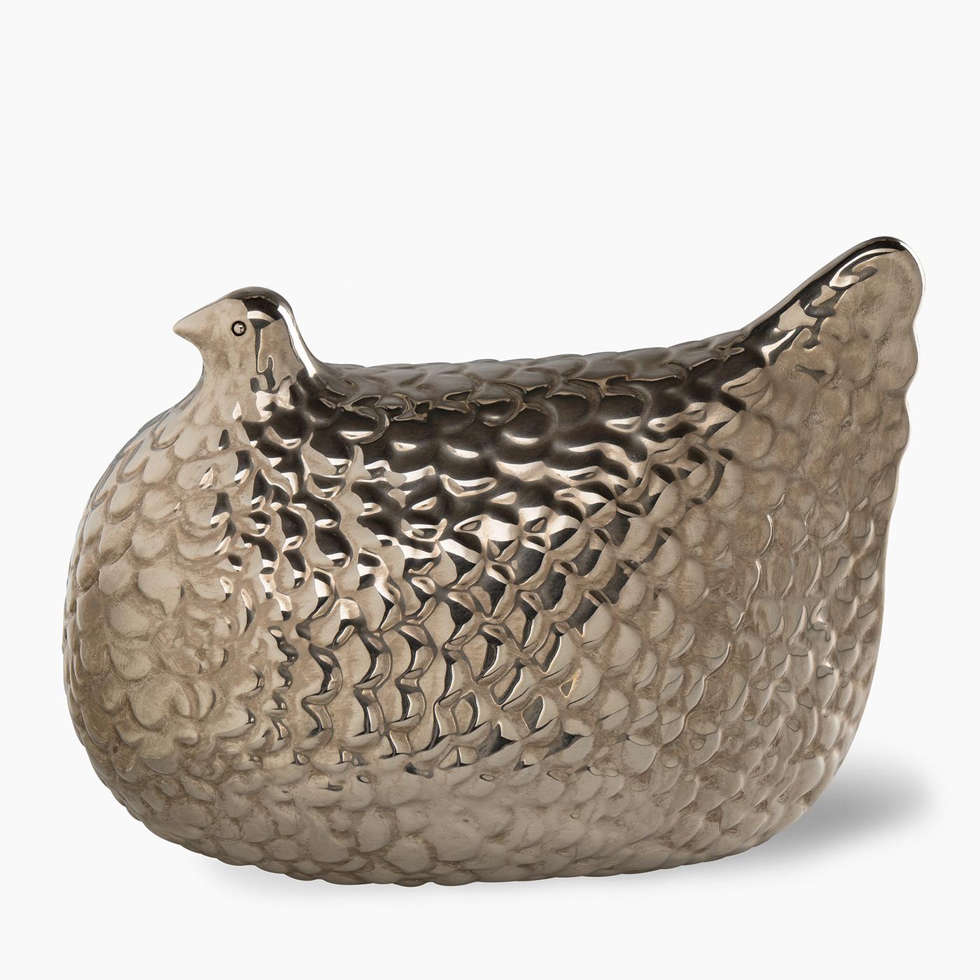 Questa statuetta in edizione limitata cattura la forma di una gallina utilizzando uno stampo in argilla rossa, rifinito con uno smalto argentato al terzo fuoco che crea una superficie riflettente e strutturata. Fa parte di una storica riedizione