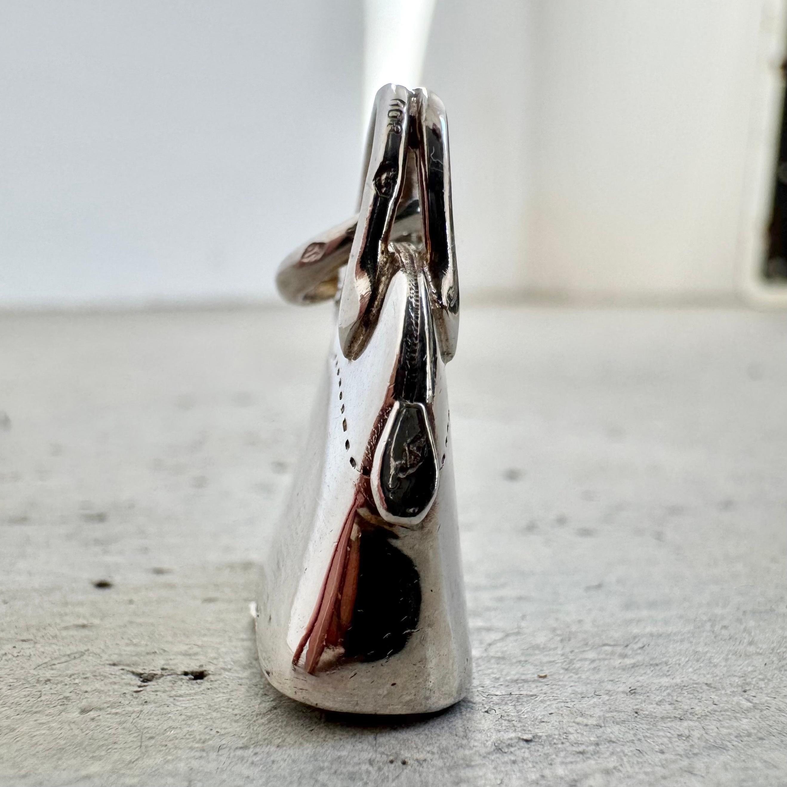 Questo piccolo charme di Hermès riprende la forma dell'iconica Borsa Bolide. Realizzato in argento sterling, il pannello inferiore di questo pezzo si apre rivelando un vano portaoggetti poco profondo. Il testo inciso sul lato recita 
