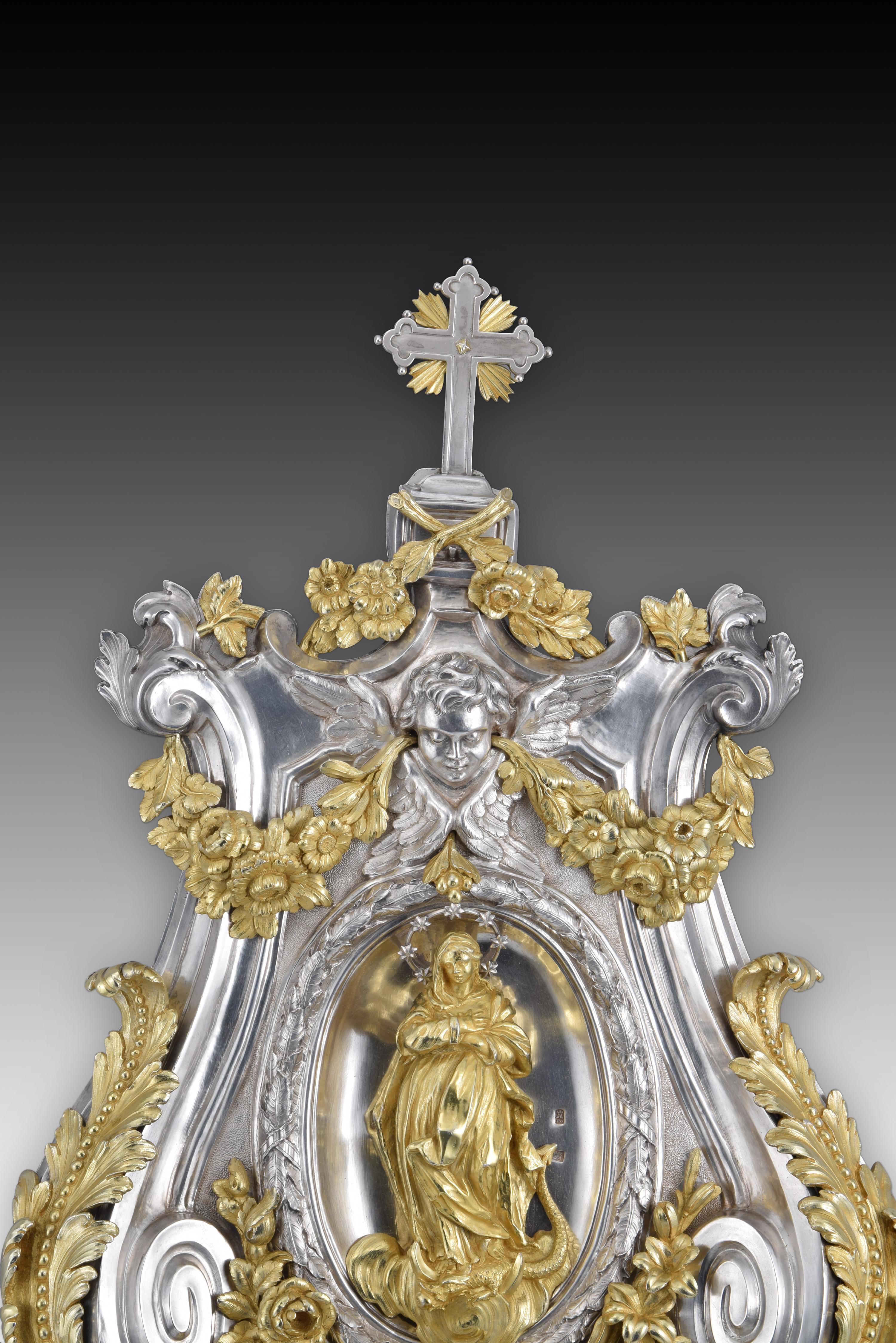 Blessing font. Silver and gilt silver. Miguel Guilla. Madrid, Spain, 1780. 
With contrast marks, buriladas and initials. 
Holy water font to be placed on the wall thanks to a chain on the back, made of silver in its color with decorative elements of