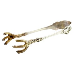 Silver ice tongs with gold claws, raised temples and grooves along the length