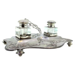Silver inkwell with two glass tanks on a base with floral reliefs on four feet