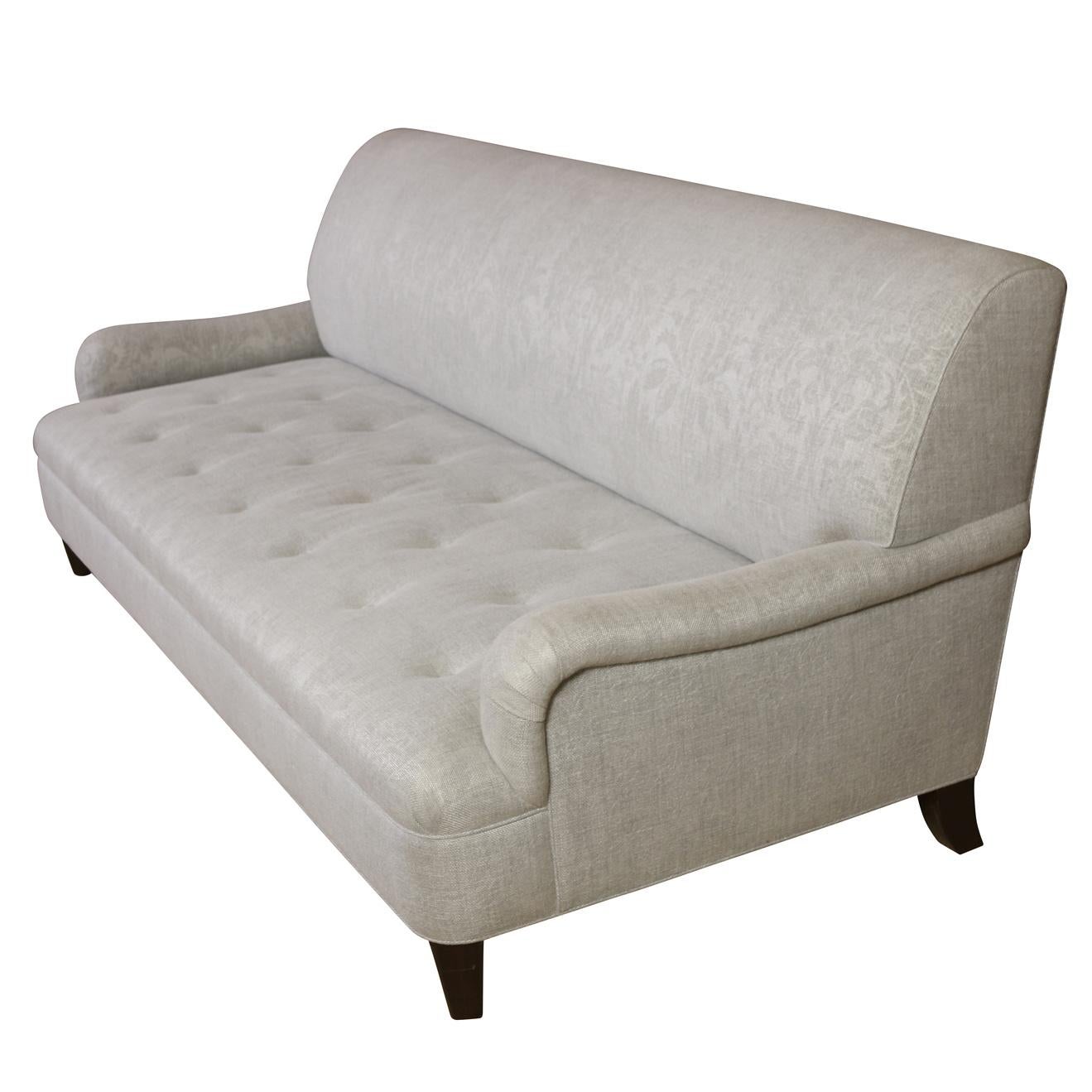 A contemporary style long sofa in silver jacquard upholstery with a tight back, tufted seat, low curved arms and wooden legs.