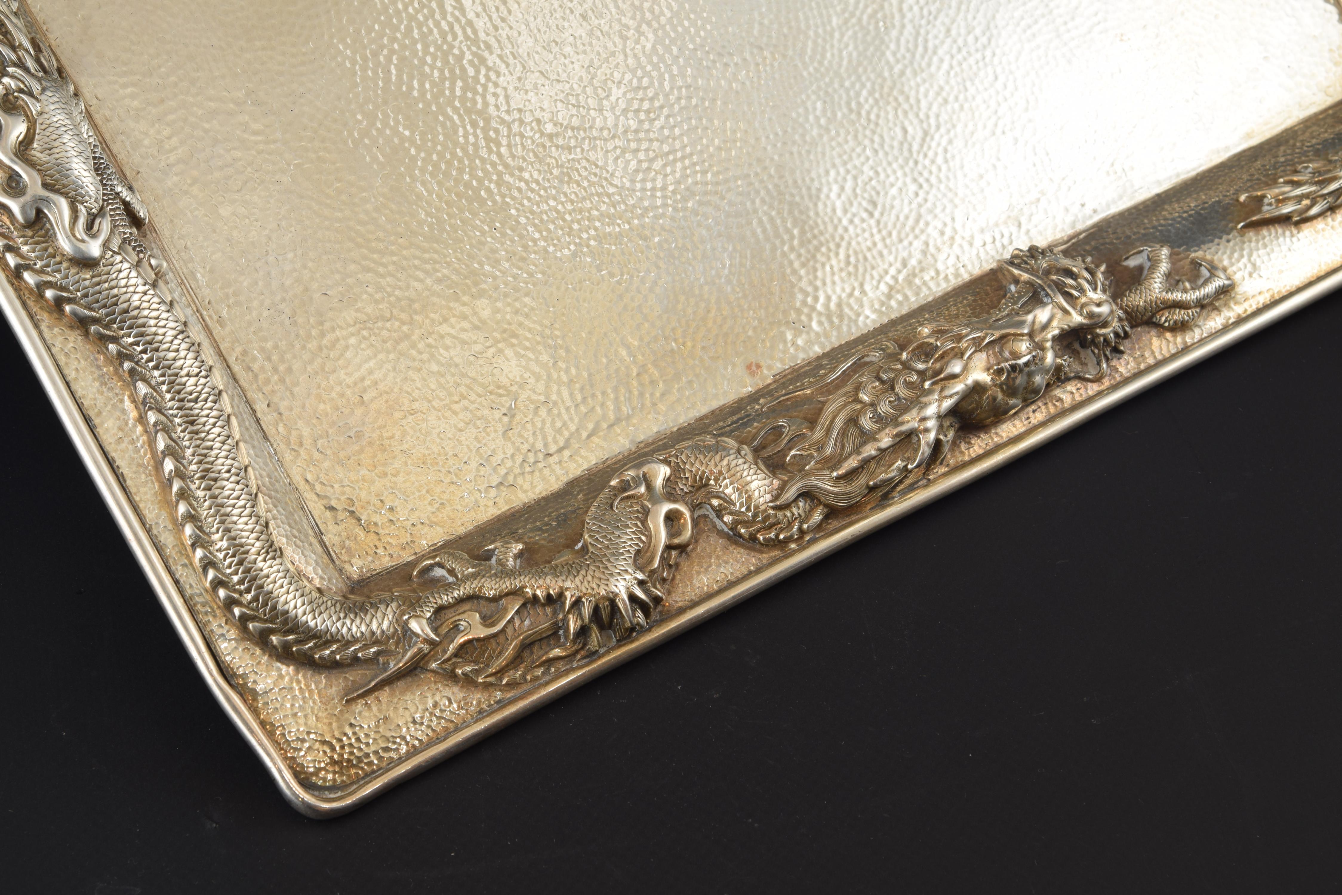 Rectangular tray made in silver and decorated, on the edge, with two dragons with three oriental claws undulating in relief, animals common in oriental art and very appreciated in the objects imported to Europe. The base has clear contrast marks