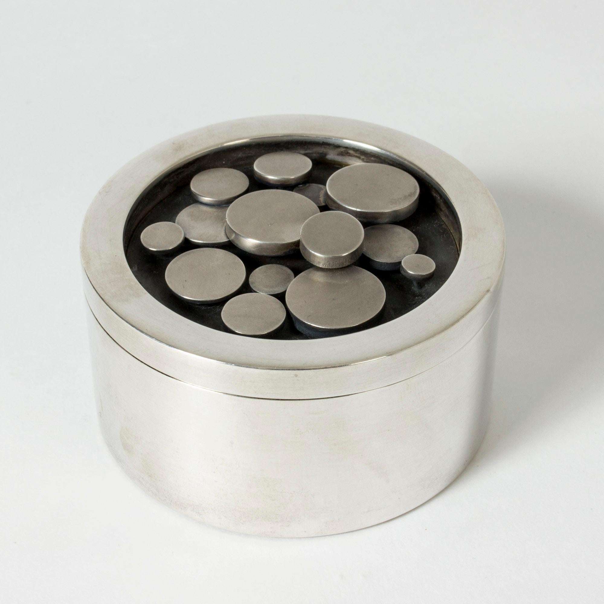 Exquisite silver jar from Atelier Borgila, with a gilded inside and a pattern of silver discs on the lid. Blackened silver backdrop to the discs.