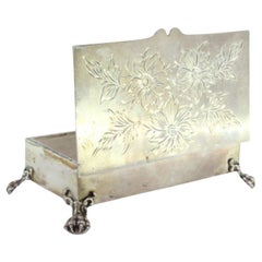 Silver jewelry box with floral lid engravings and four claw-shaped feet