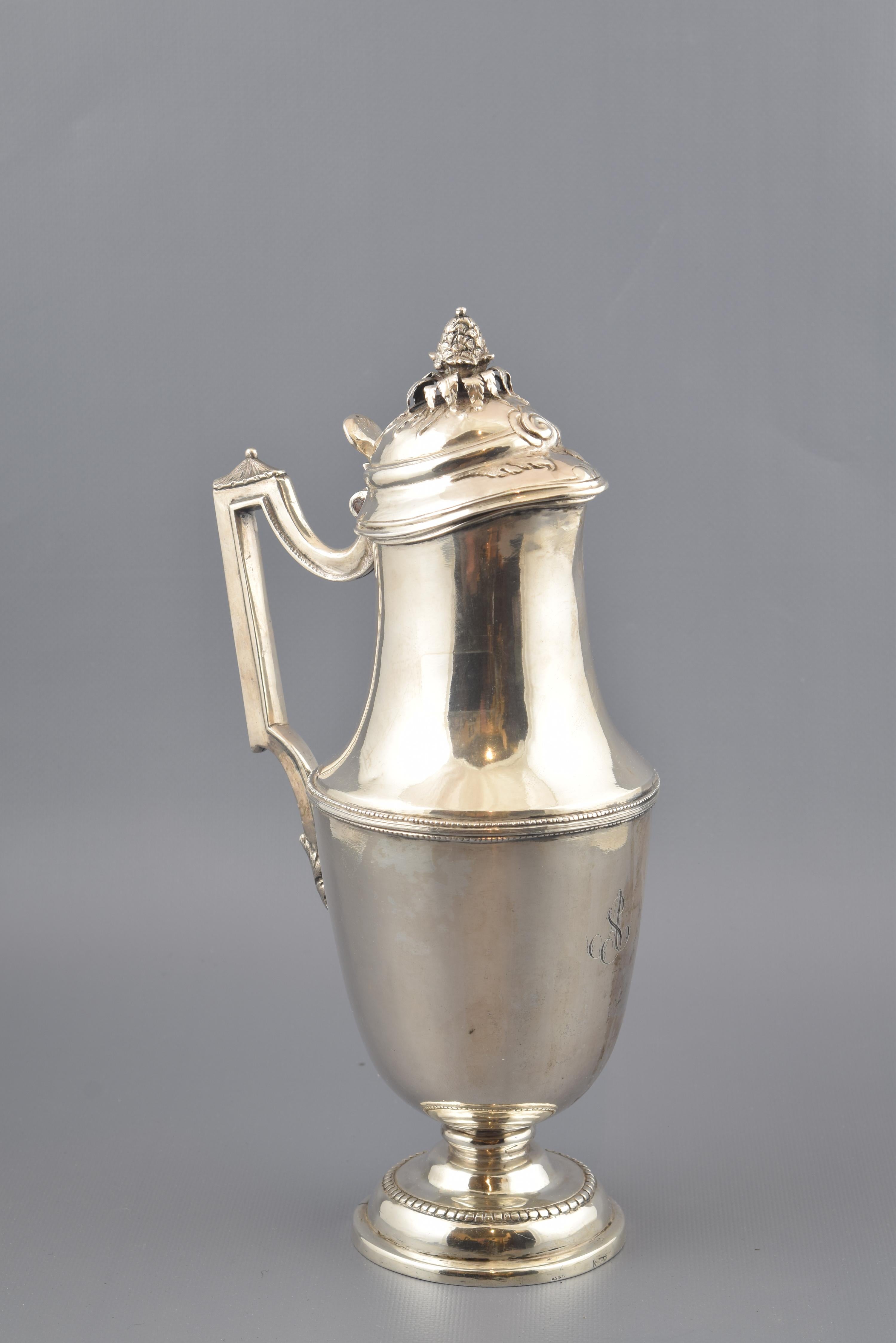Jug with lid and silver handle in its color that has a circular foot decorated and raised with a series of moldings and a band of pearls, from which part a small foot that gives way to the body of the piece (oval in the lower area and curved in the