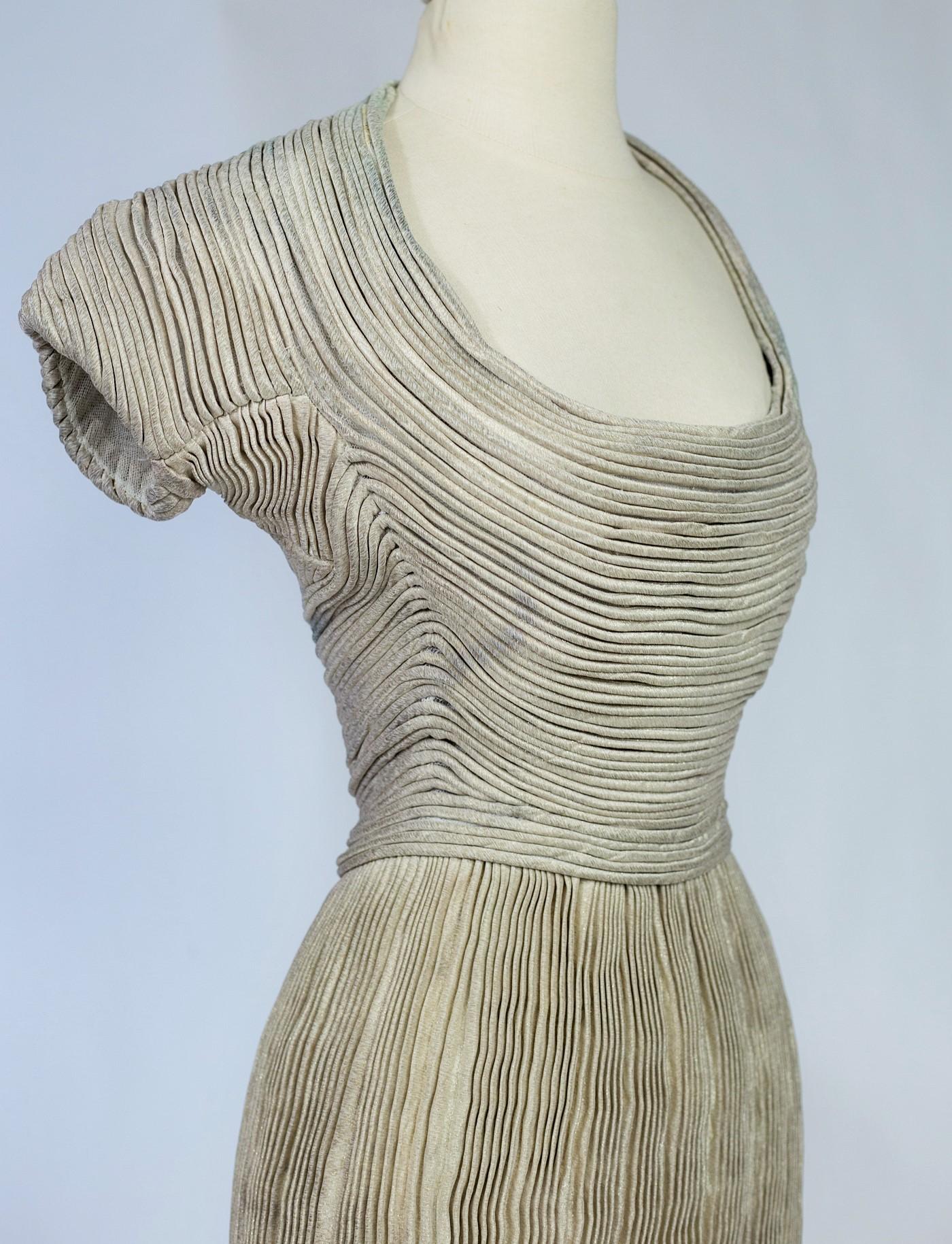 Circa 1940
France
Sculptural silver lamé evening dress with a large oval neckline and small kimono sleeves by Lucile Manguin, member of the French haute couture union and daughter of the painter Fauve, dated 1938 - 1942. Amazing work of quilting