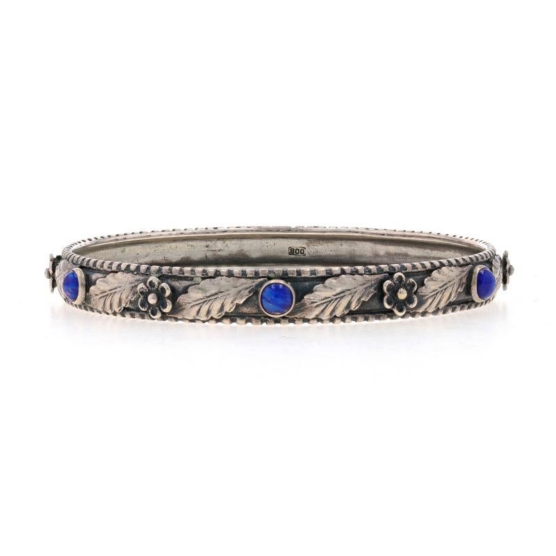 Era: Vintage

Metal Content: 800 Silver

Stone Information
Natural Lapis Lazuli
Cut: Round Cabochon
Color: Blue

Style: Bangle
Fastening Type: N/A (slides over wrist)
Theme: Flower Garland

Measurements
Inner Circumference: 7 3/4