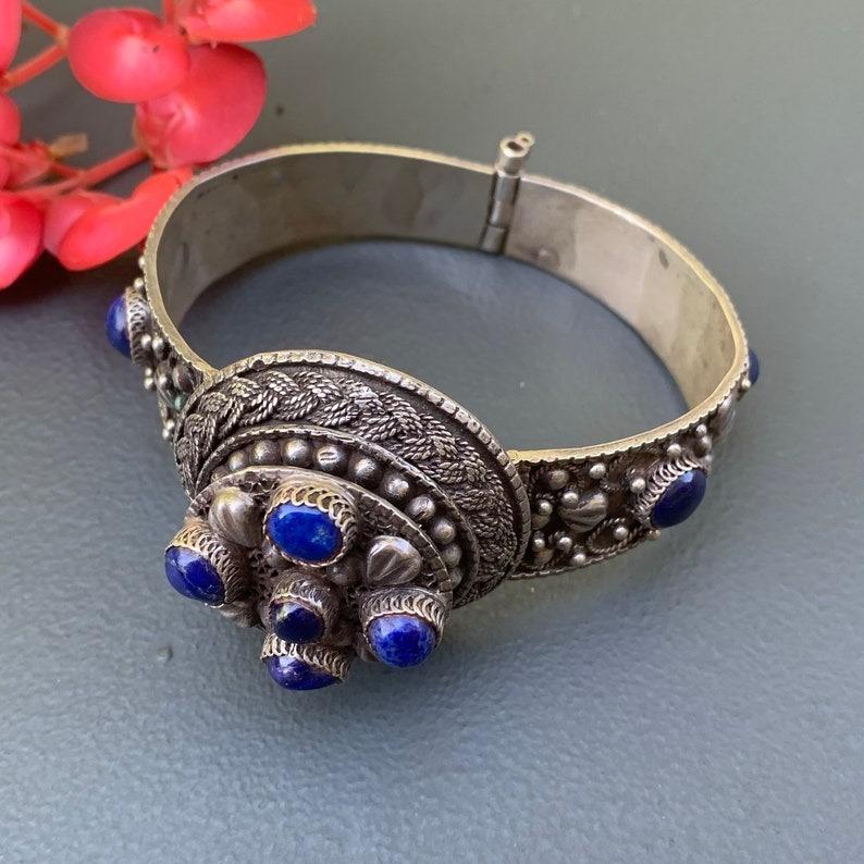 Il bracciale vintage presenta una splendida pietra di lapis incastonata in argento con un disegno di fiori e foglie applicato. La parte superiore del bracciale si apre per rivelare uno scomparto segreto con cerniera, perfetto per contenere un