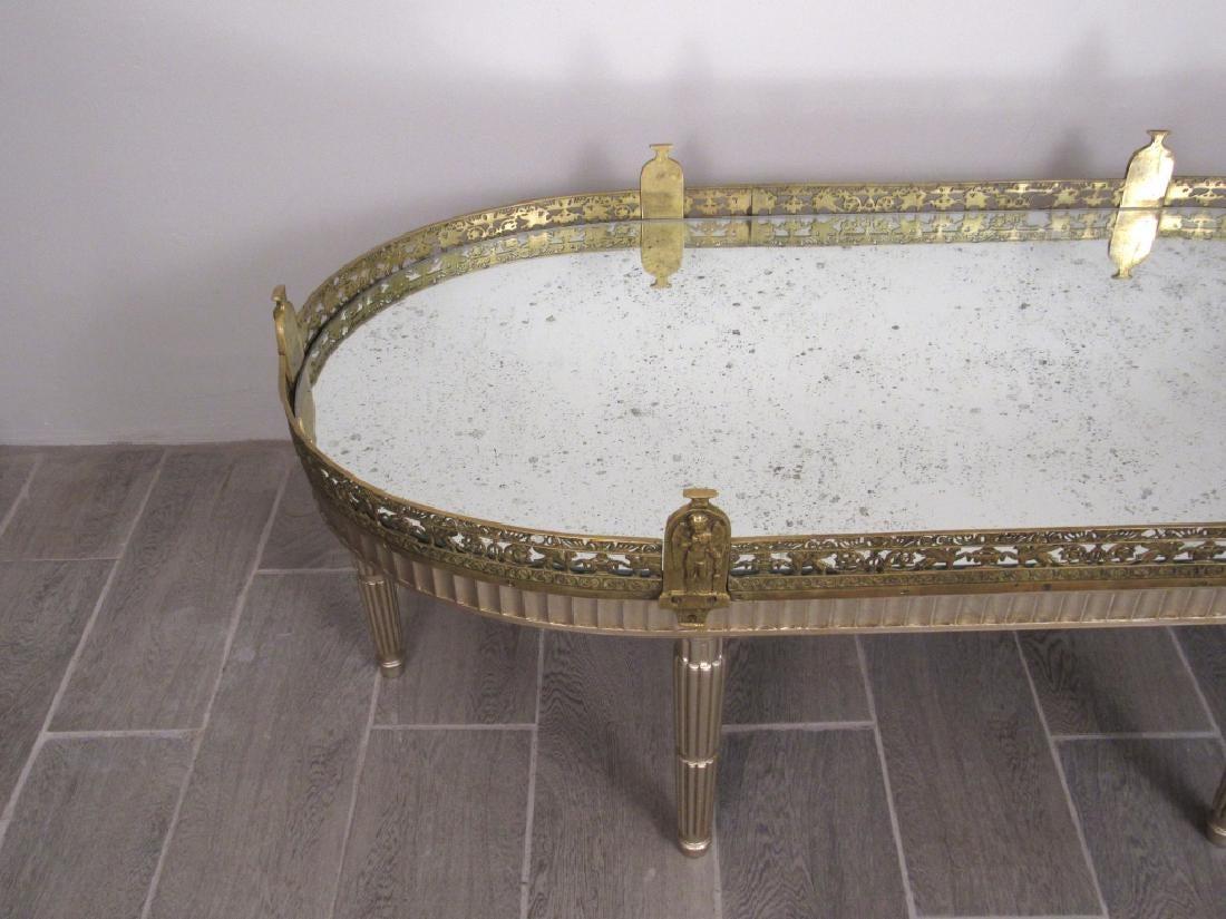 Neoclassical style cocktail table with antiqued mirrored top. Silver leaf French Louis XVI style gilt bronze mirrored plateau or coffee table. The antiqued mirrored top with a bronze gallery having griffins and angel post. Silvered fluted base with