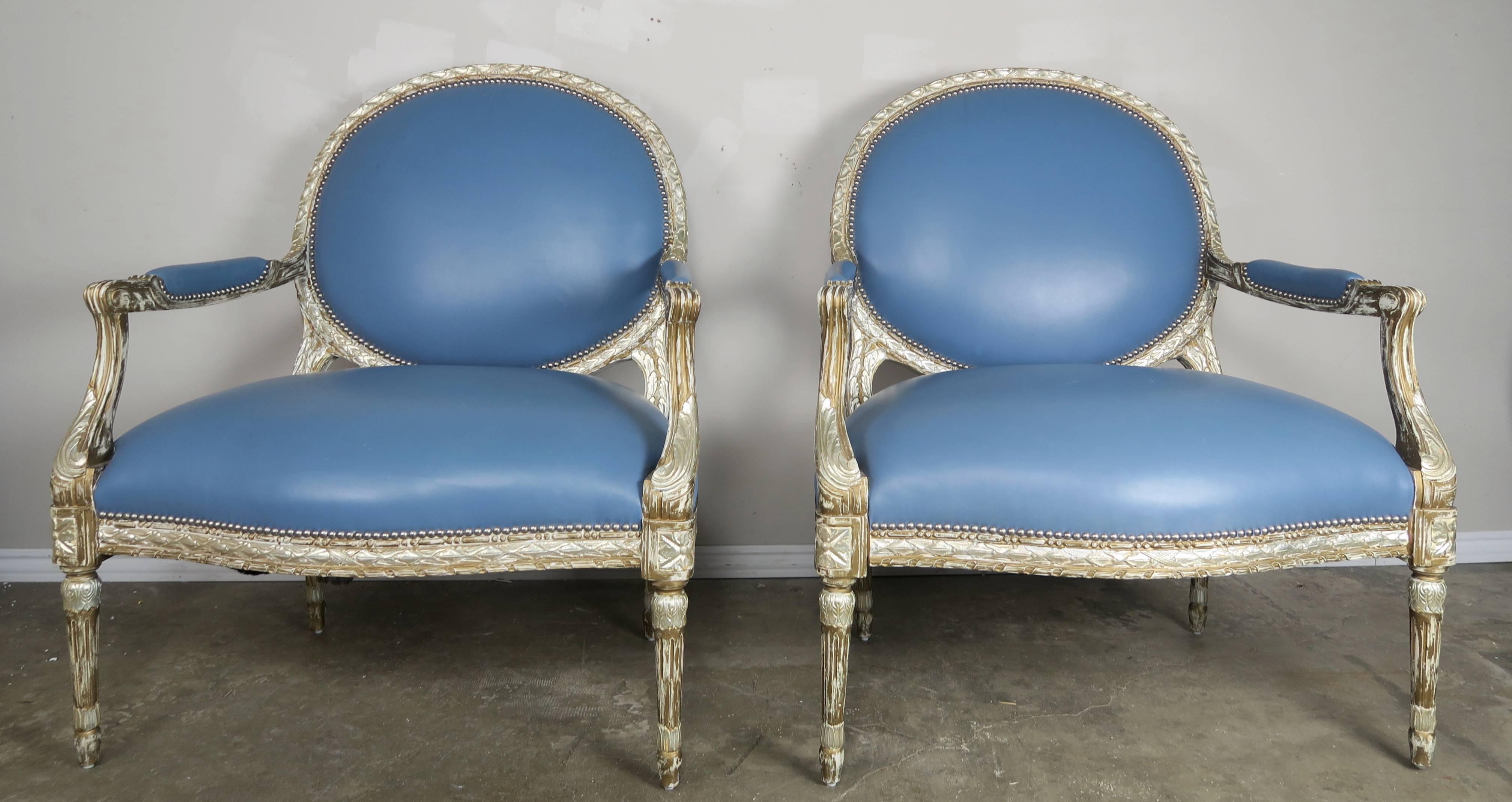 Pair of beautifully carved neoclassical style designer silver gilt armchairs upholstered in blue leather with nailhead trim detail.
 