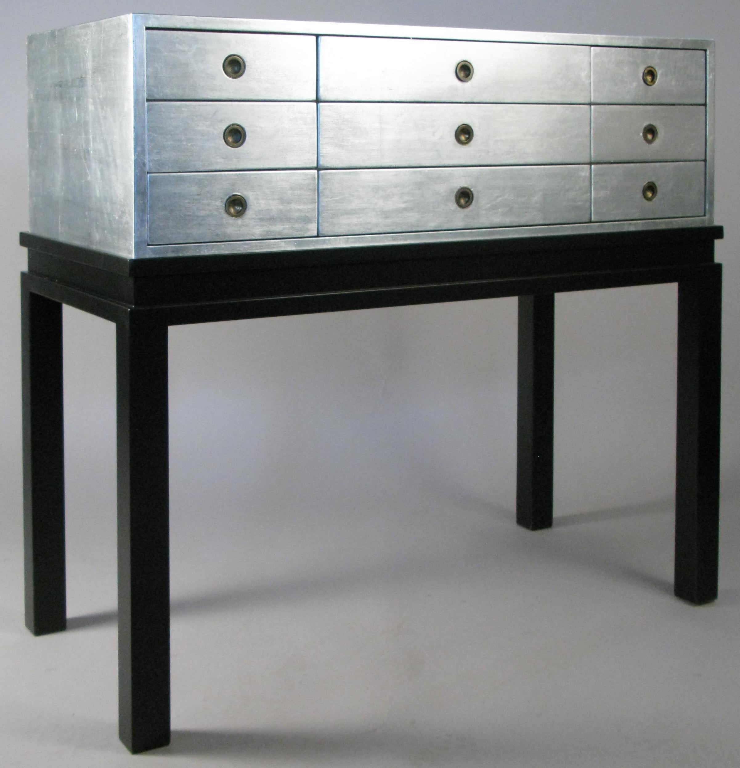 An outstanding vintage 1960s nine-drawer chest by Kittinger. The case fitted with nine drawers with recessed brass ring pulls, finished in beautiful silver leaf. The case rests upon a black lacquered base. Perfect for a wide variety of placements,