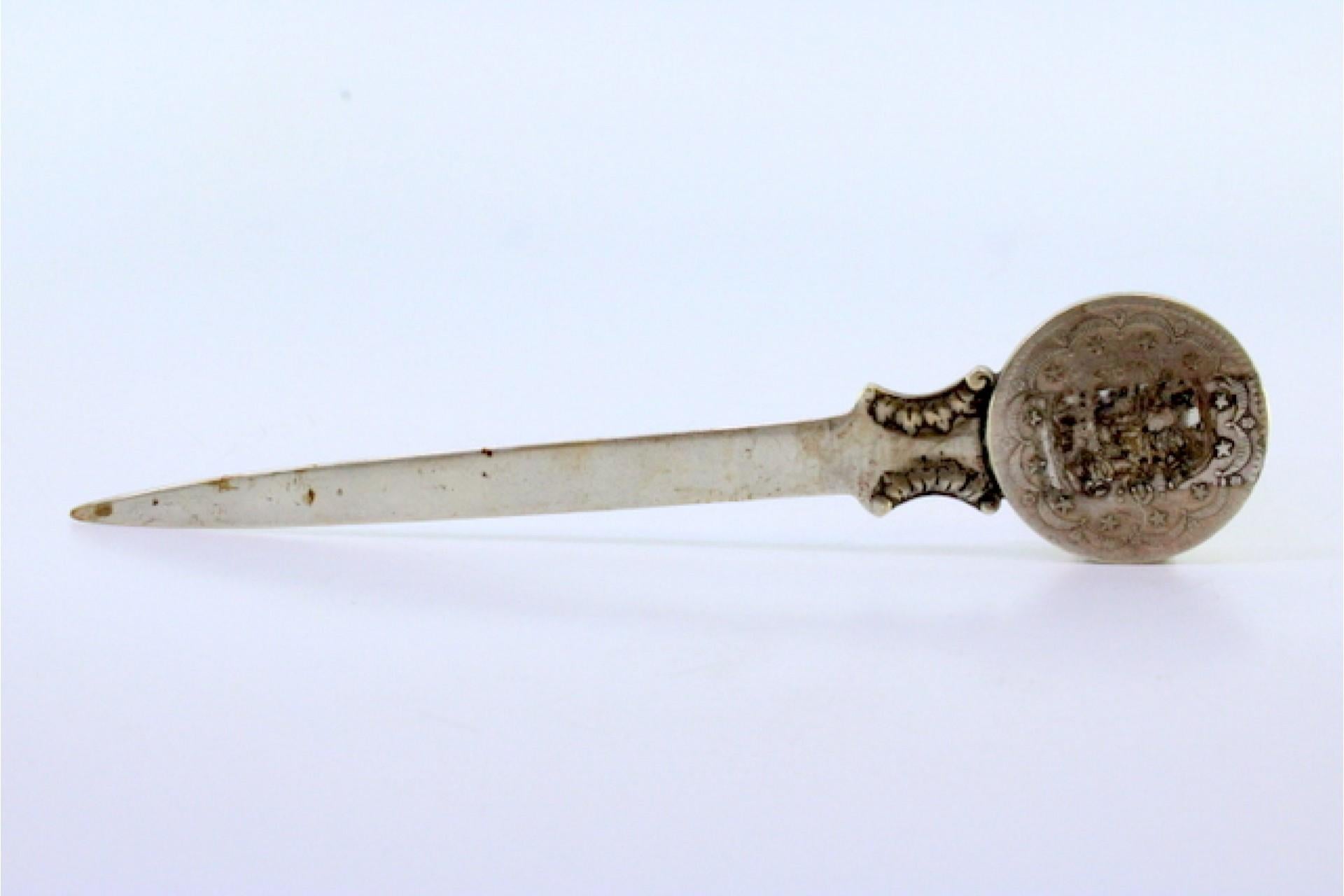 Beschreibung: Silberner Brieföffner mit arabischer Münze auf der Oberseite und Reliefs. 
Metall: Silber. 
Herkunft: Arabisch. Marke: Unbekannt. 
Gewicht: 35,51 Gramm. 
Abmessungen: 16,7x3,7cm. 
Inhalt: 800/1000. 
Prüfzeichen: Ja. 
Zusätzliche
