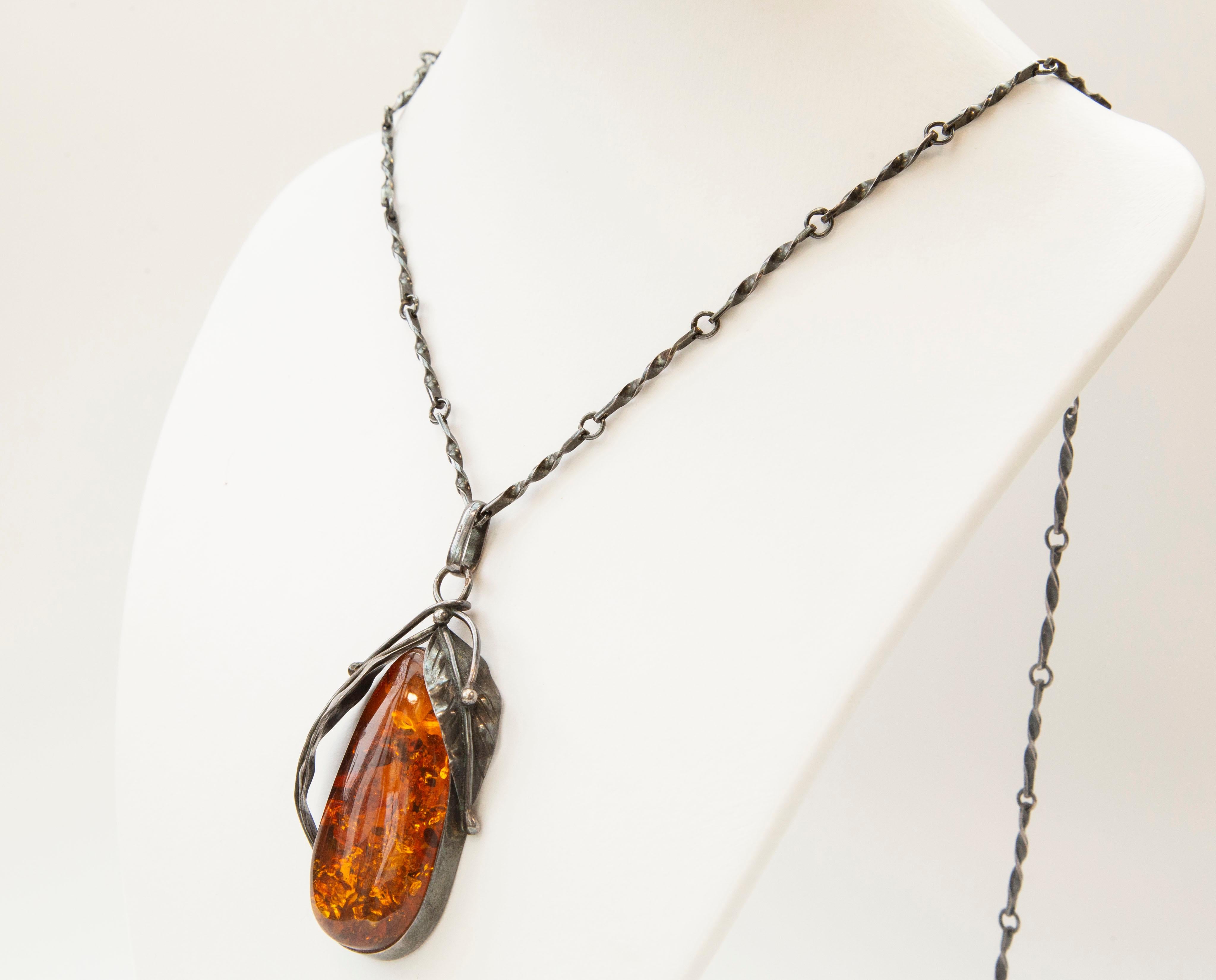 A vintage hand crafted pendant with a silver link necklace. The pendant is made from a drop shaped amber cabochon and it is in an oval silver frame decorated with silver leaves. 
The necklace and the pendant are marked KS, there are also other marks