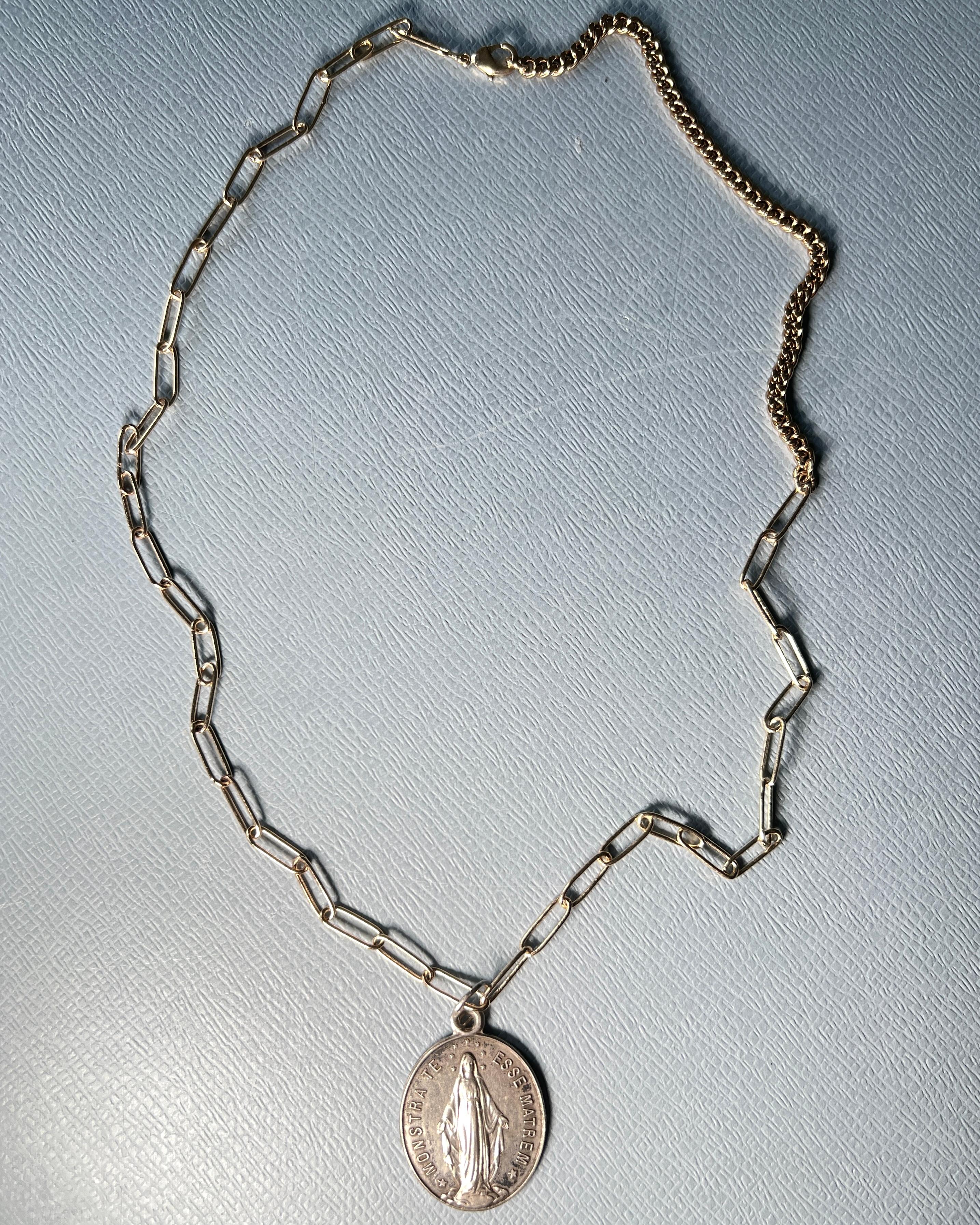 This vintage French religious medal necklace features a finely detailed Virgin Mary pendant inscribed with the Latin invocation Monstra Te Esse Matrem — Show Thyself as Mother. The medal is an original antique, cast in solid silver, and paired with