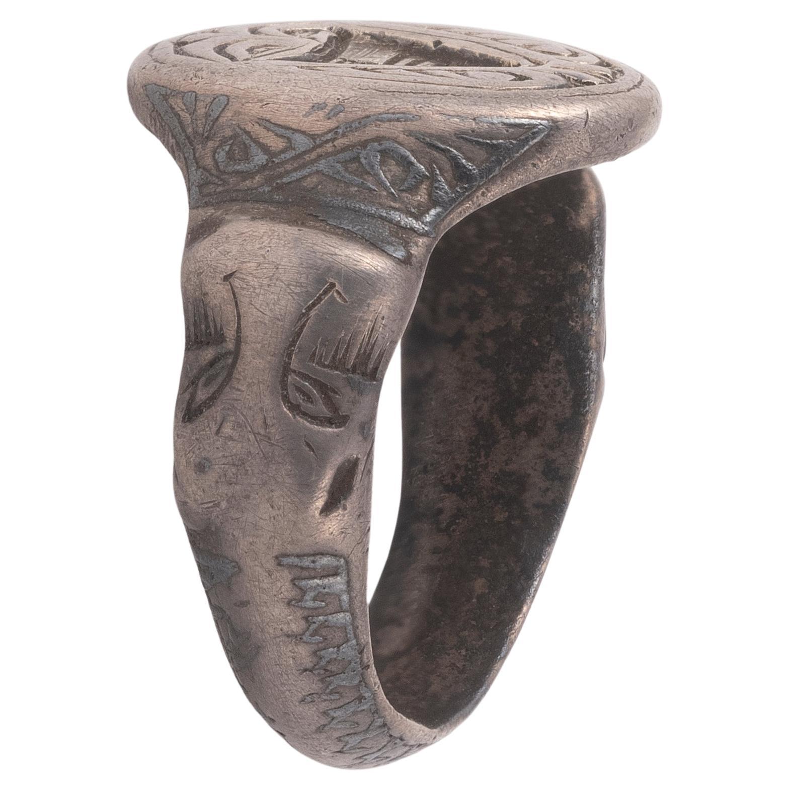 A medieval merchant’s silver ring with an oval bezel, depicting a coat of arms. The shield at the centre appears to be quartered, with the top left and bottom right featuring horizontal lines. The shoulders of the ring are stepped and decorated with