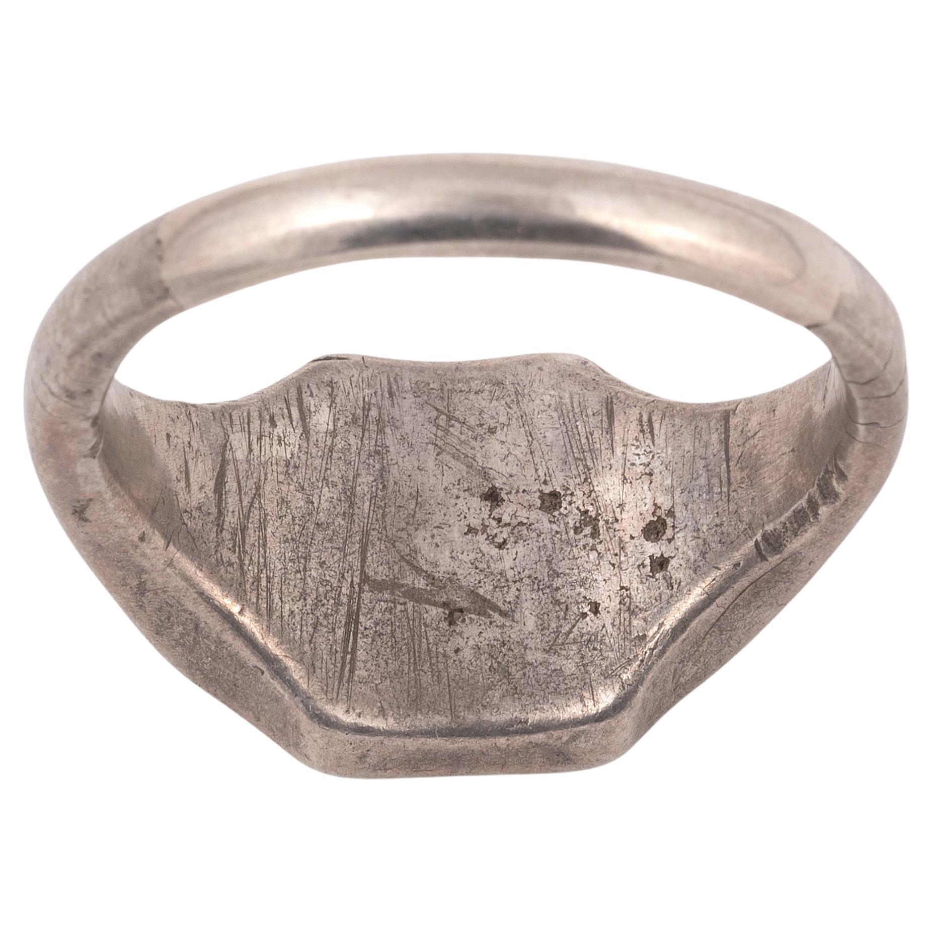 A medieval silver merchant's seal ring with a flat sectioned round hoop that enlarges on the shoulders to form a hexagonal bezel. The seal on the bezel depicts a shield with an armoured arm holding a sword, a popular heraldic device in Eastern