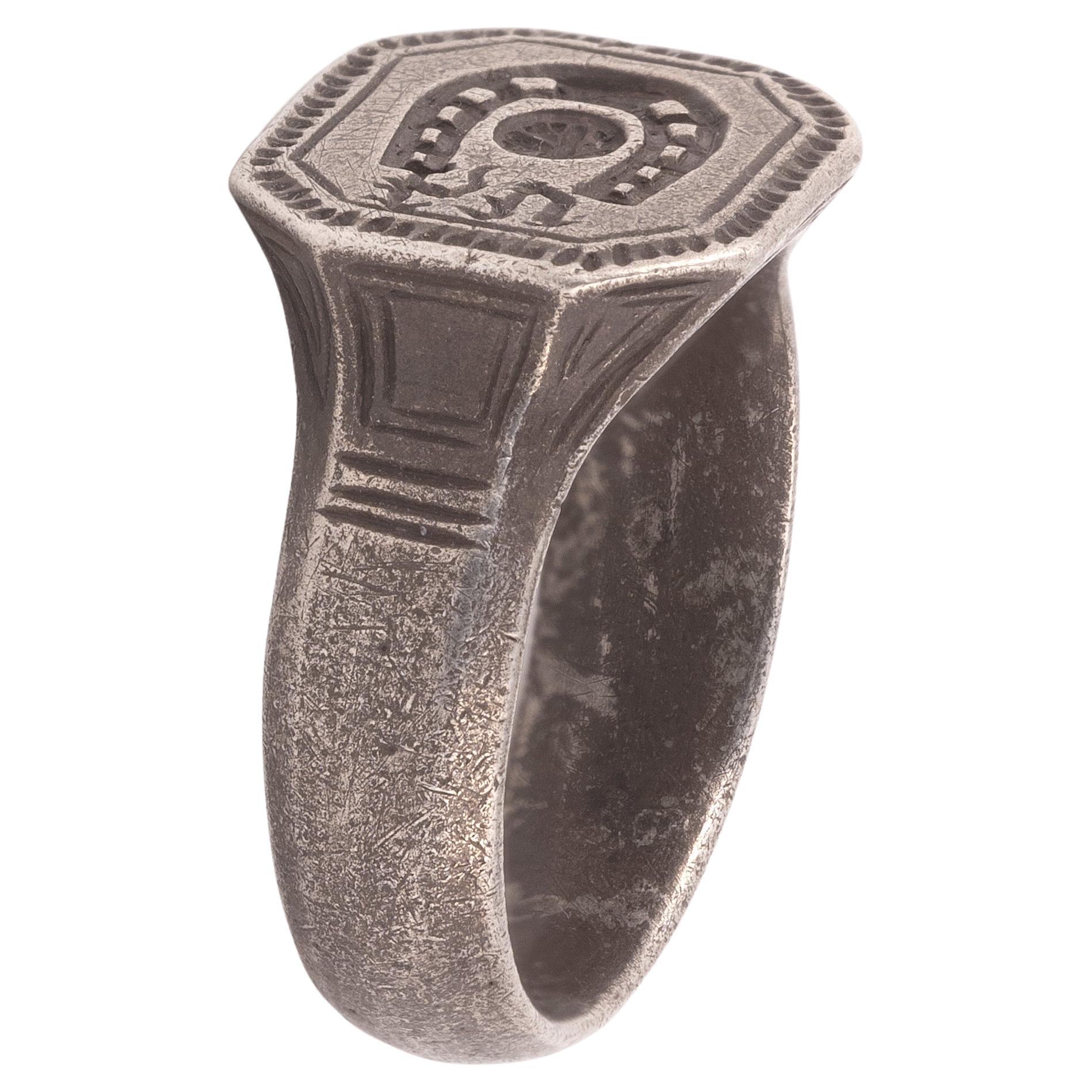 A medieval silver ring with a high octagonal bezel, depicting a horseshoe, a cross within a circle and the initials H. V. In heraldry, horseshoes are often used in the arms of families with names like Farrier, Marshall, and Smith. The bezel is