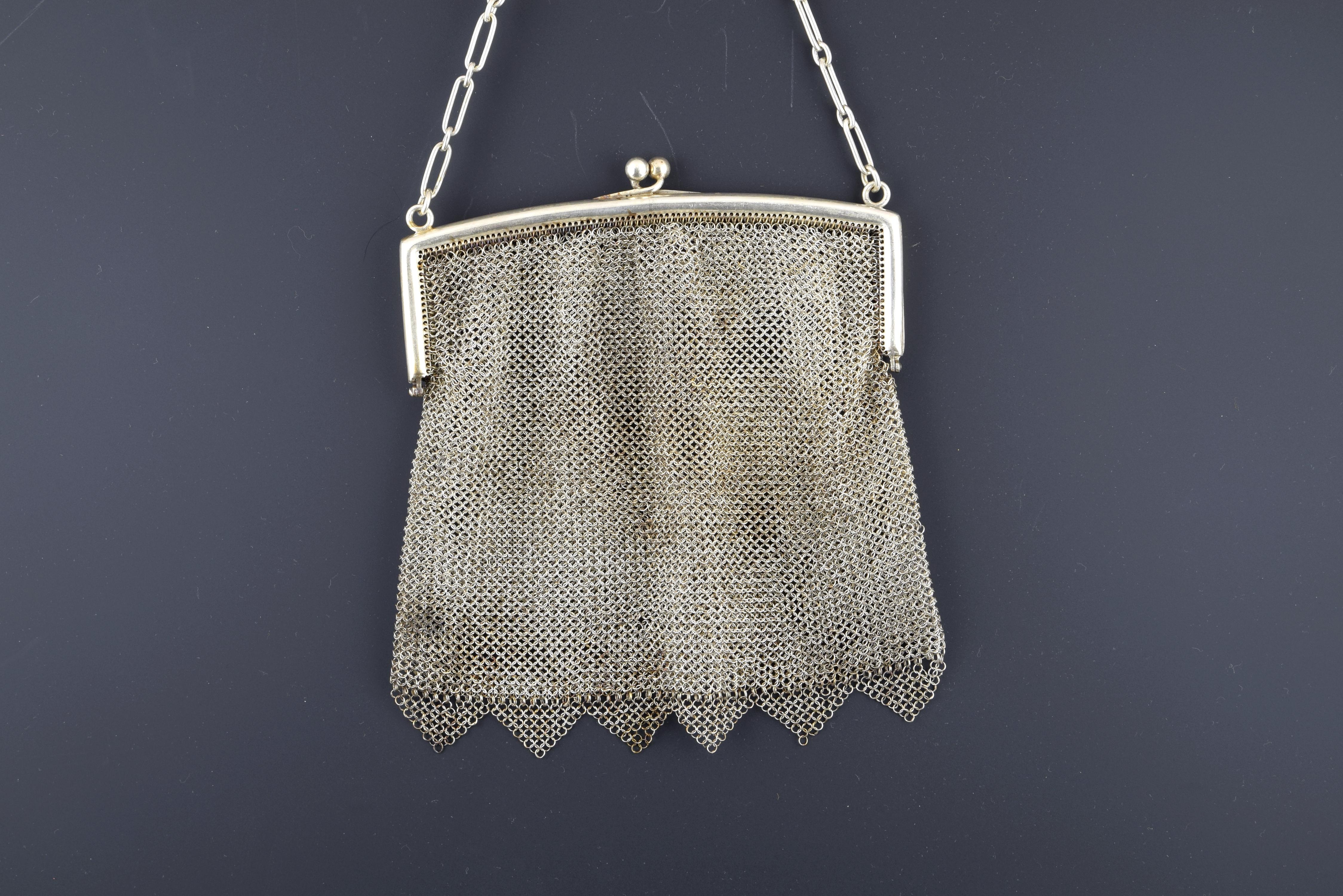 Silver mesh bag in its color decorated with triangular elements on the bottom that has a smooth closure by hinges and a chain of alternating long and short links. This type of pieces were very frequent in the 19th century, as a luxury element and a