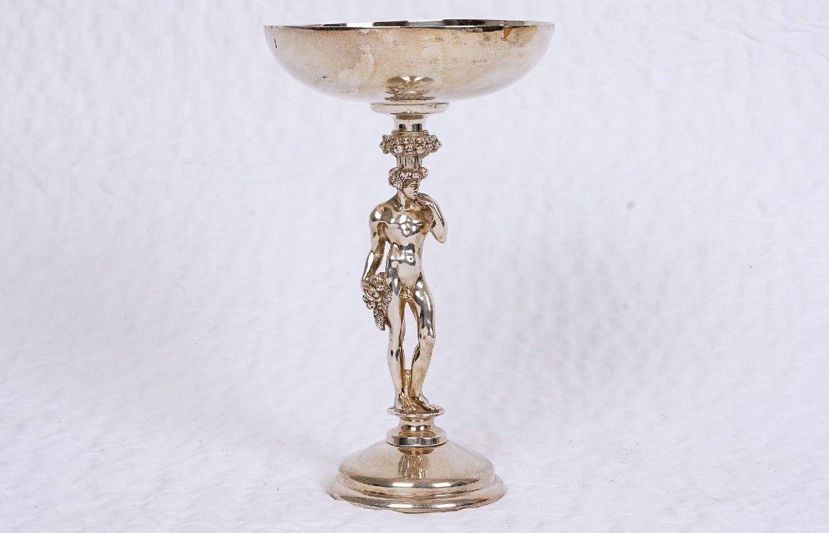 This beautiful silver-plated bowl from Christofle features a statuette of Bacchus standing on a pedestal. 
Bacchus is the god of wine in Roman mythology. He is also the god of many elements, including the vine. 
He is the god of fertility,