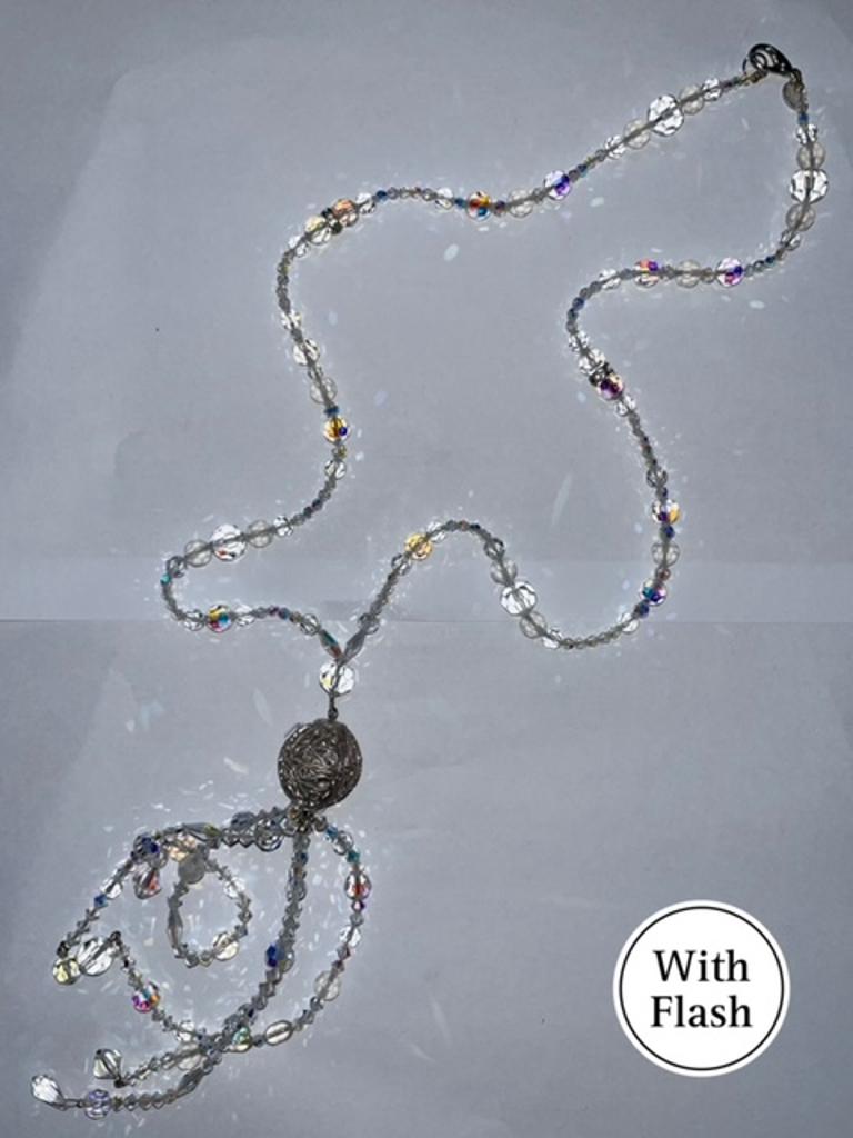 This exquisite long drop necklace is a timeless piece of intricate craftsmanship. At its centre, a beautifully detailed silver-toned spherical pendant features delicate arabesque motifs, adding a touch of vintage refinement.  The necklace is